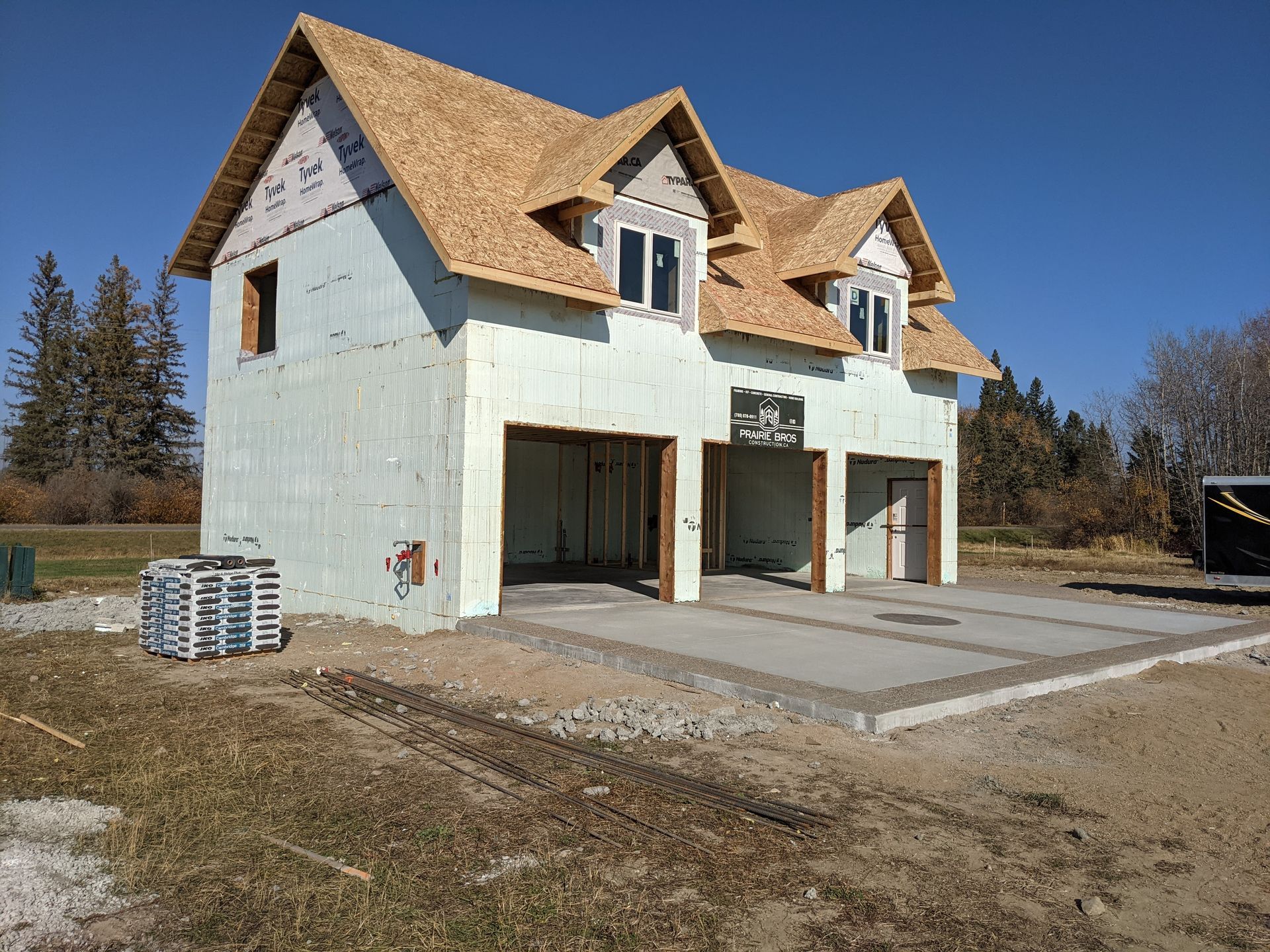 Construction site: Two-story building with garage bays, tan roof, light green walls, on a concrete pad, blue sky.