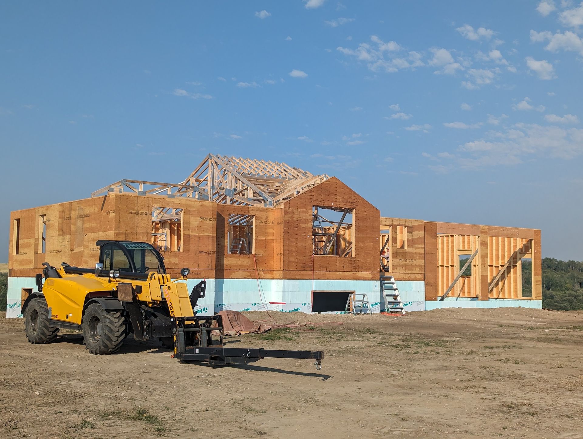 A yellow forklift is parked in front of a house under construction