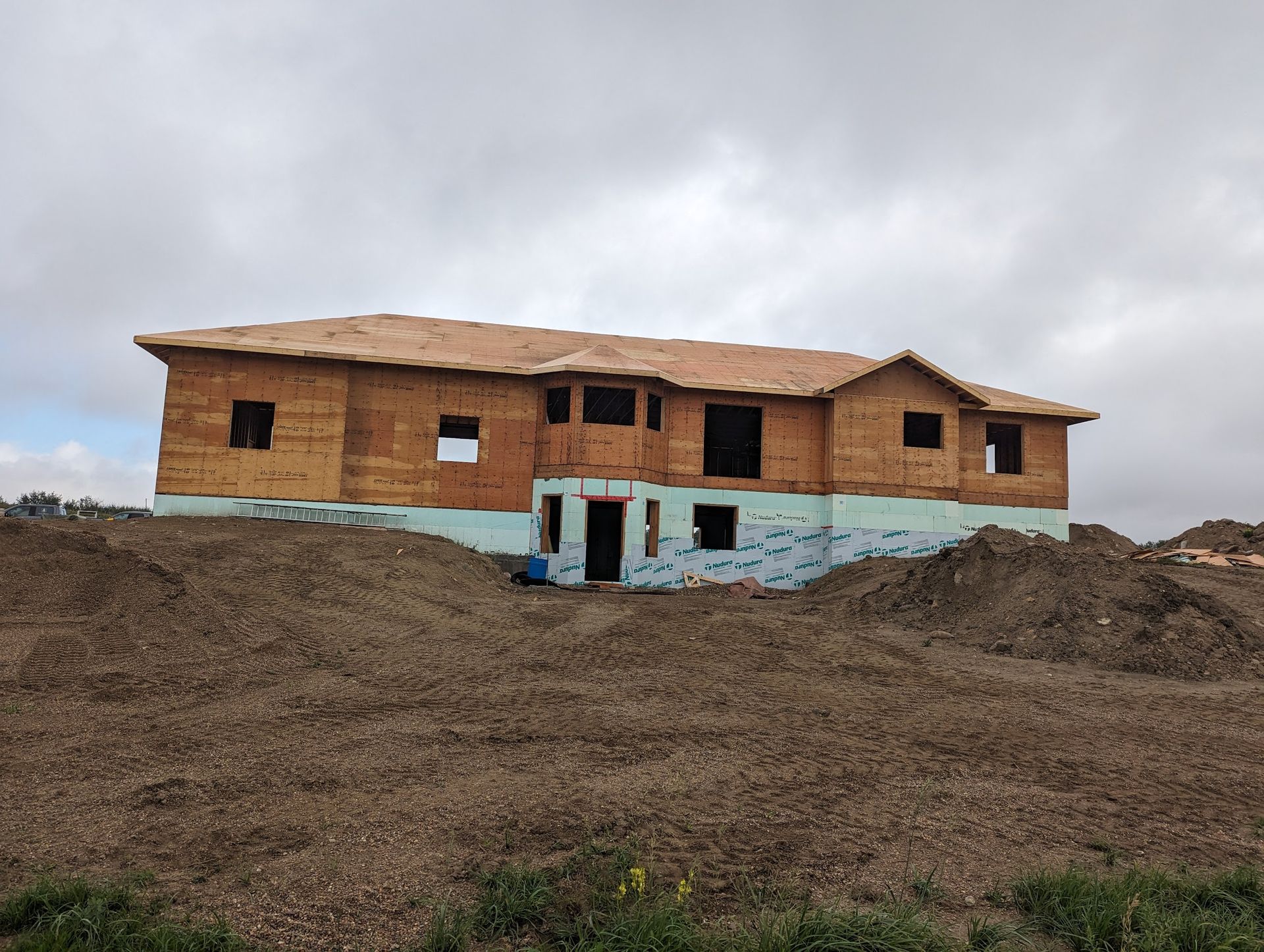 A large wooden house is being built on top of a dirt hill.
