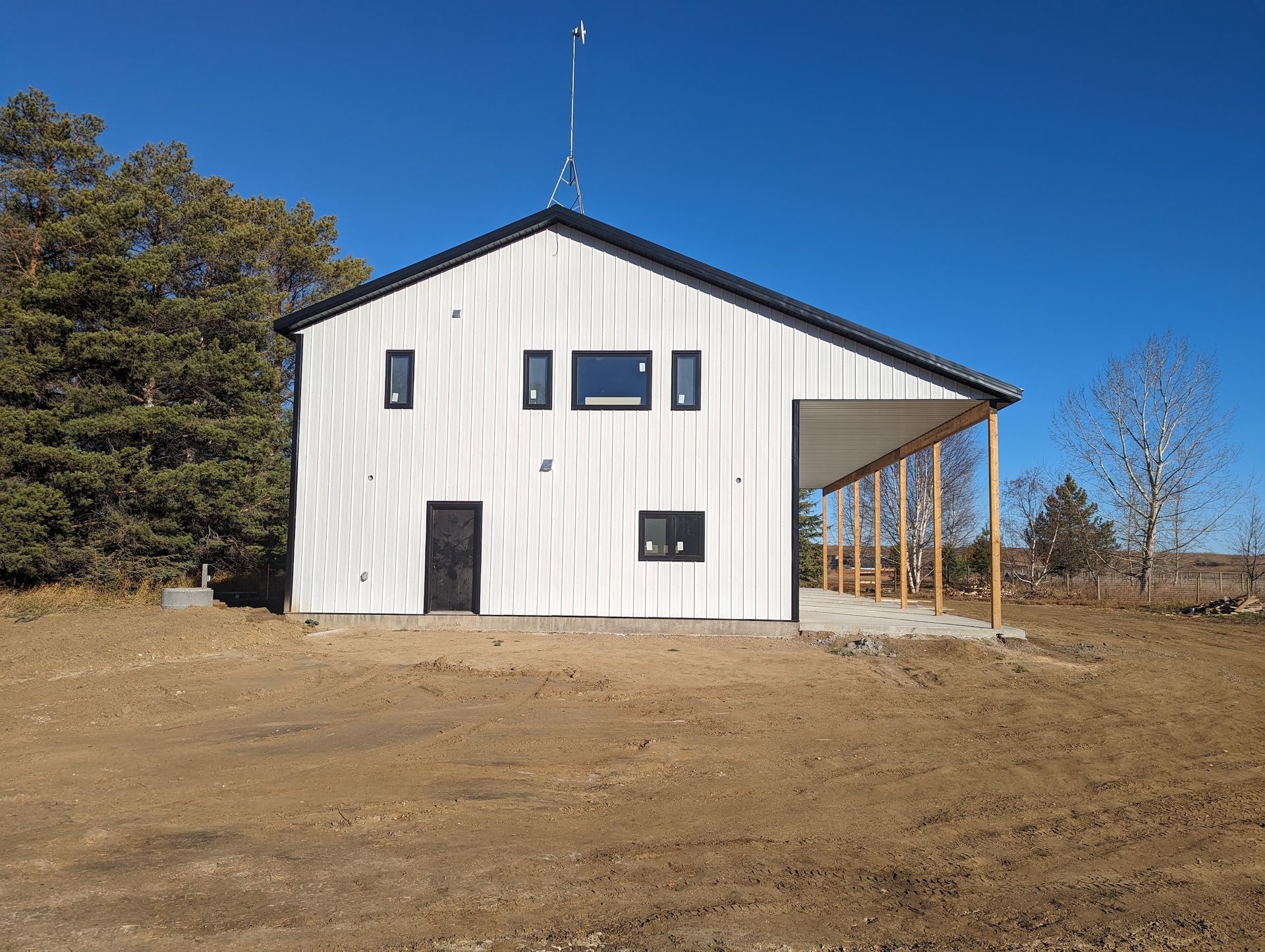 A white building with a black roof is sitting in the middle of a dirt field.