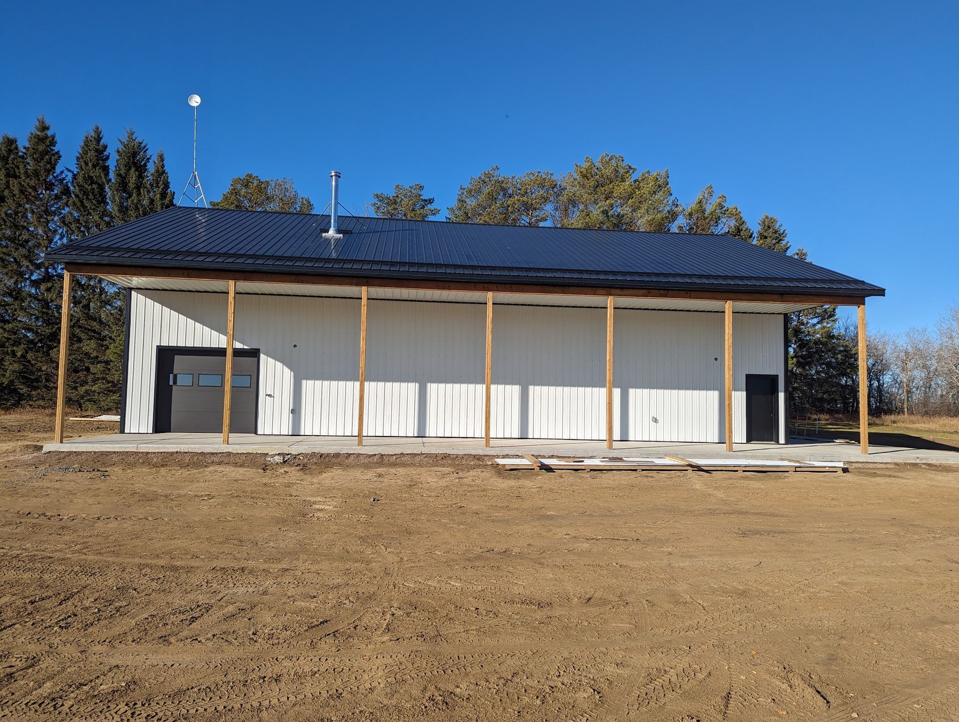 A large white building with a black roof is sitting in the middle of a dirt field.