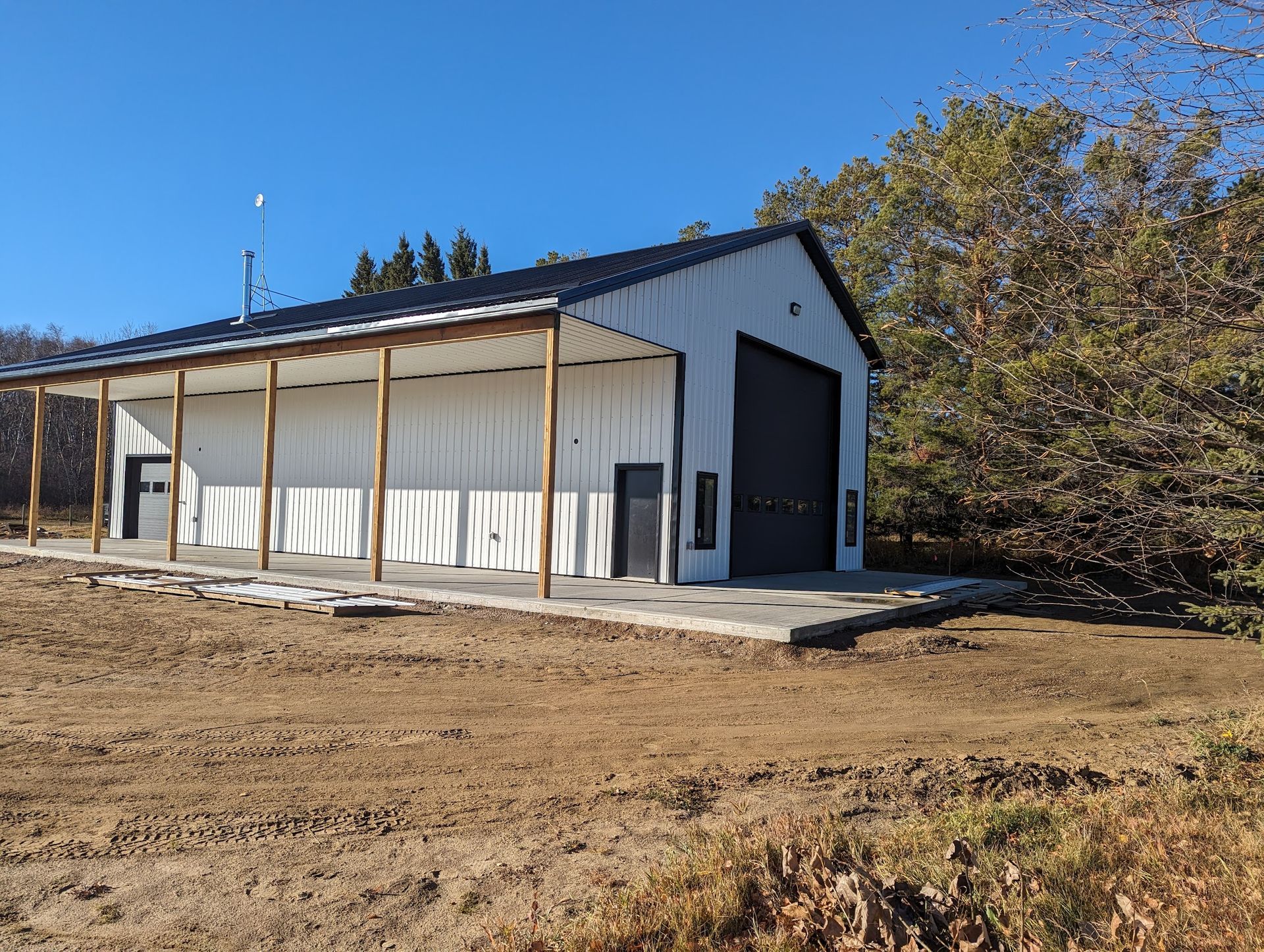 A large white building with a black roof is sitting in the middle of a dirt field.