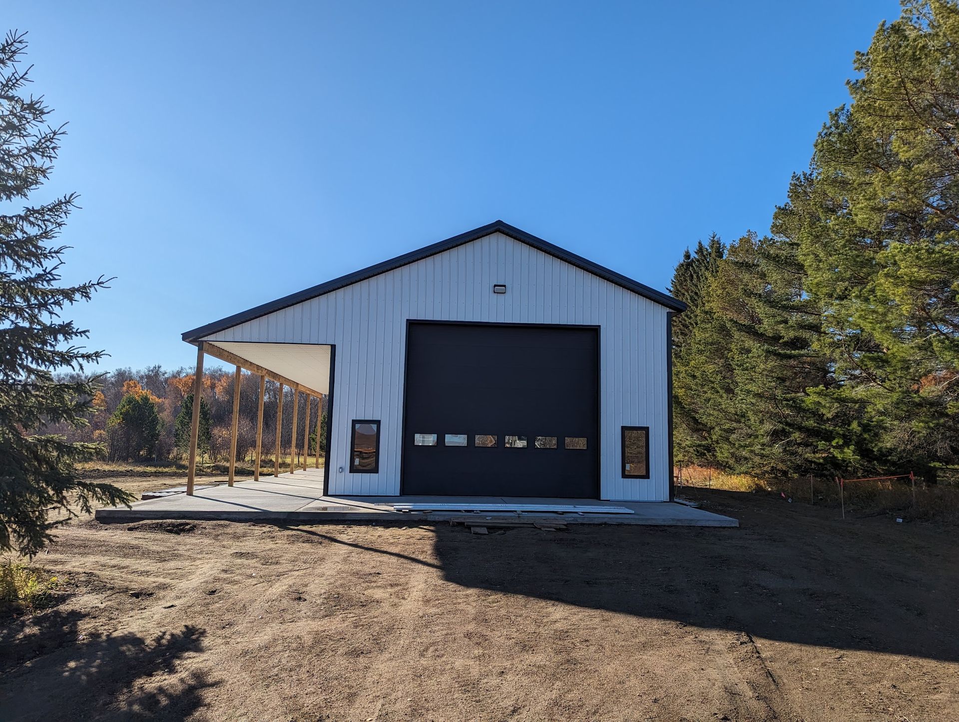 A white garage with a black door is sitting in the middle of a dirt field.