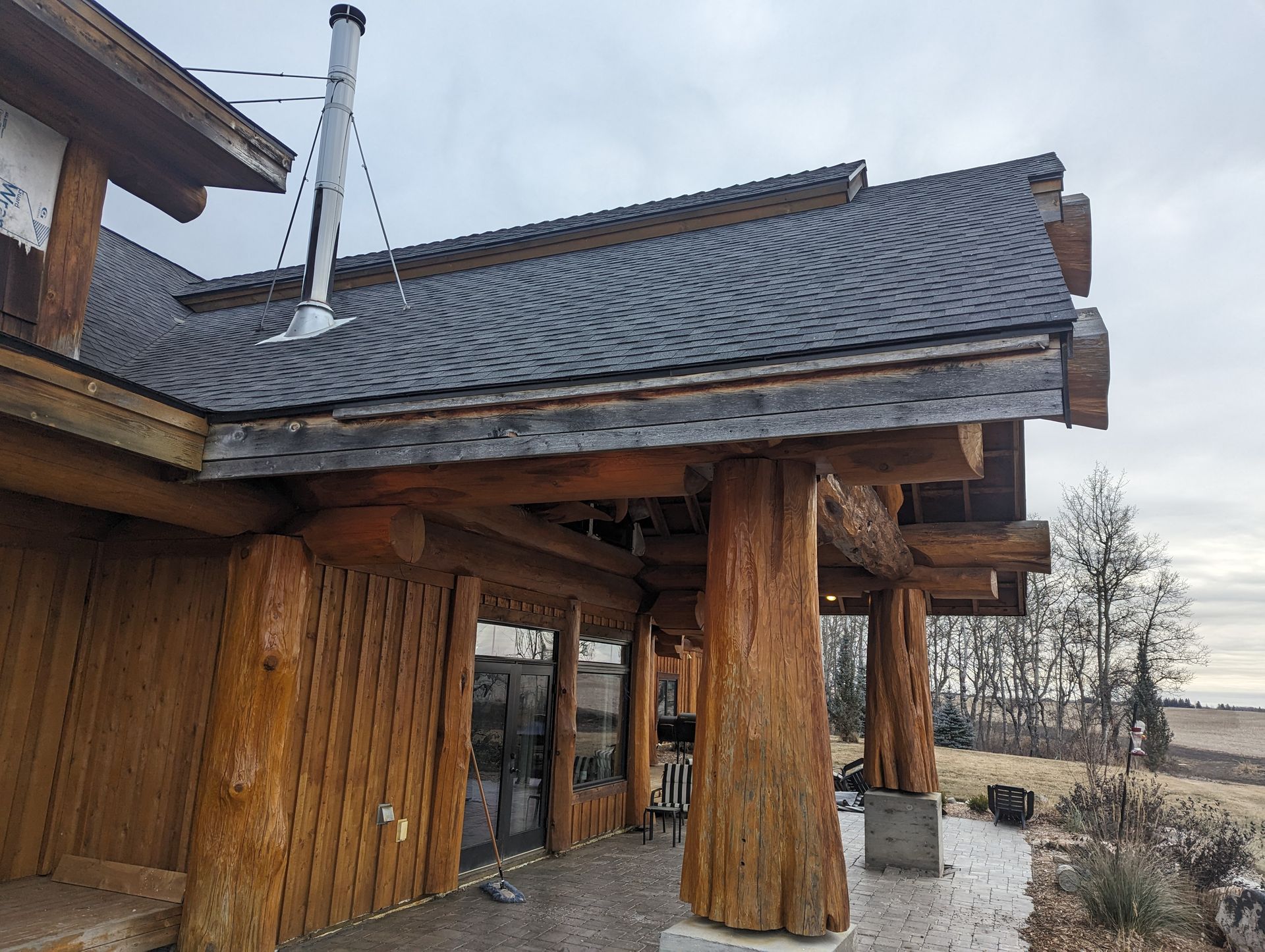 Log cabin exterior with wooden pillars, gray roof, and chimney against a cloudy sky.