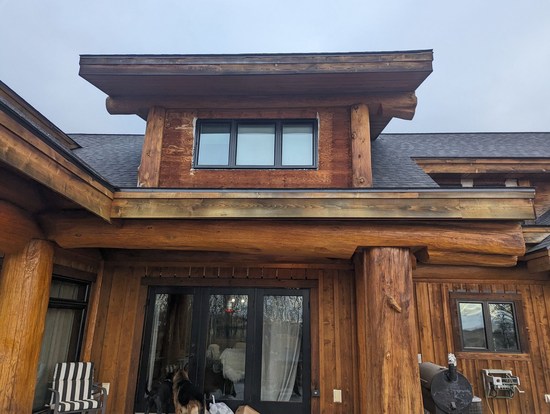 Wooden cabin exterior with window, dark roof, and log beams.