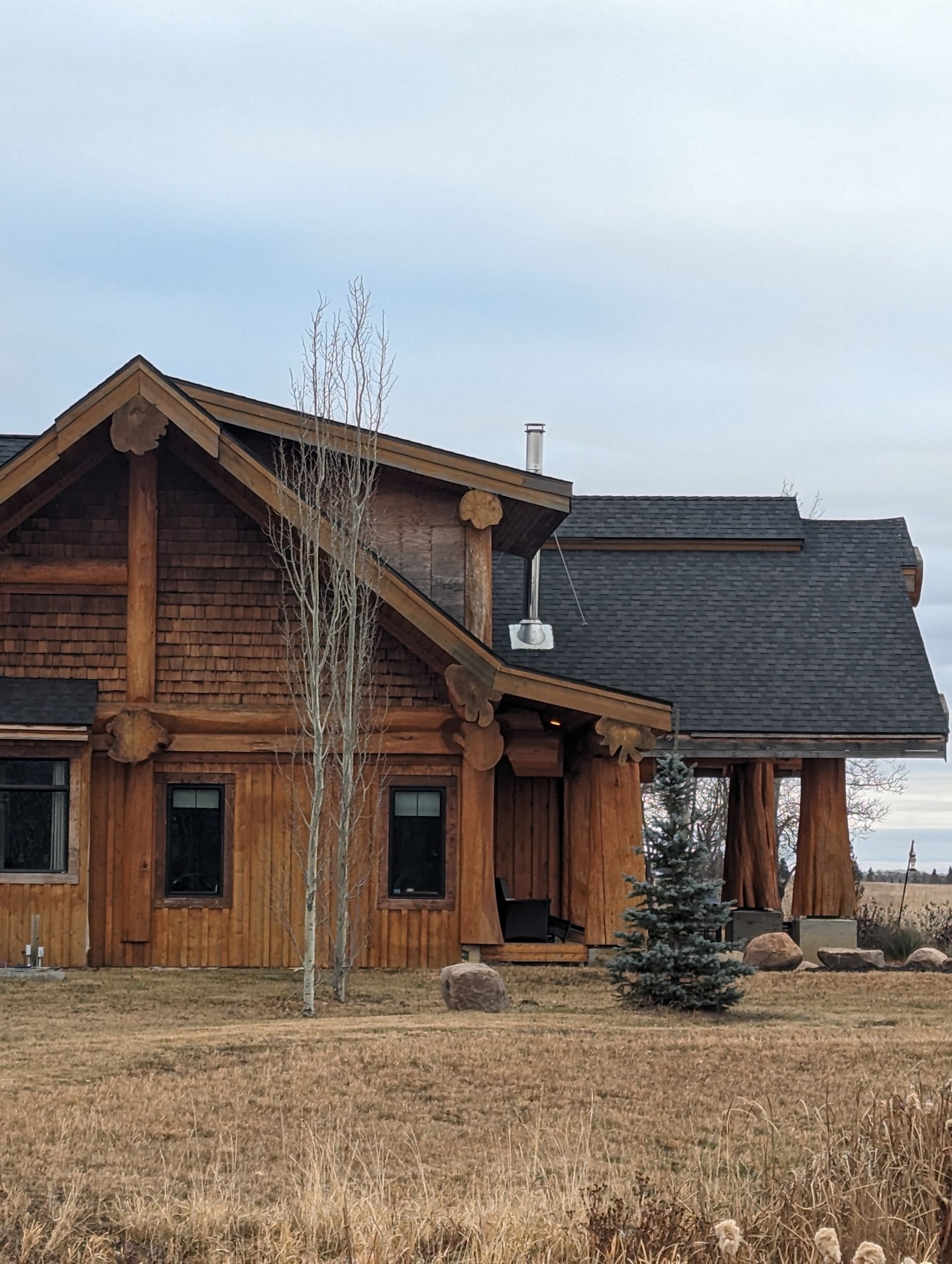 Wooden cabin with black roof, small windows, and light brown dry grass in front.