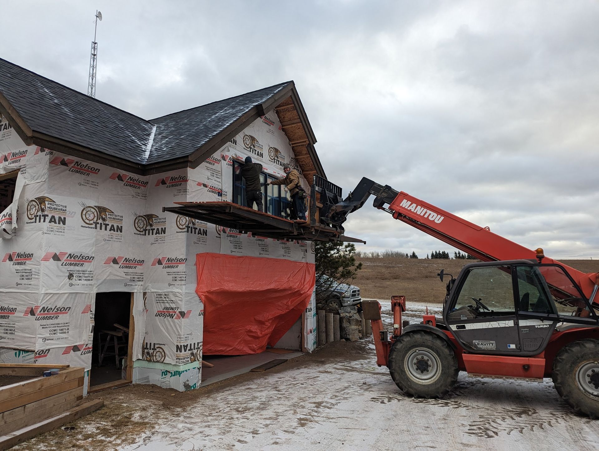 A red forklift is lifting a roof of a house under construction.