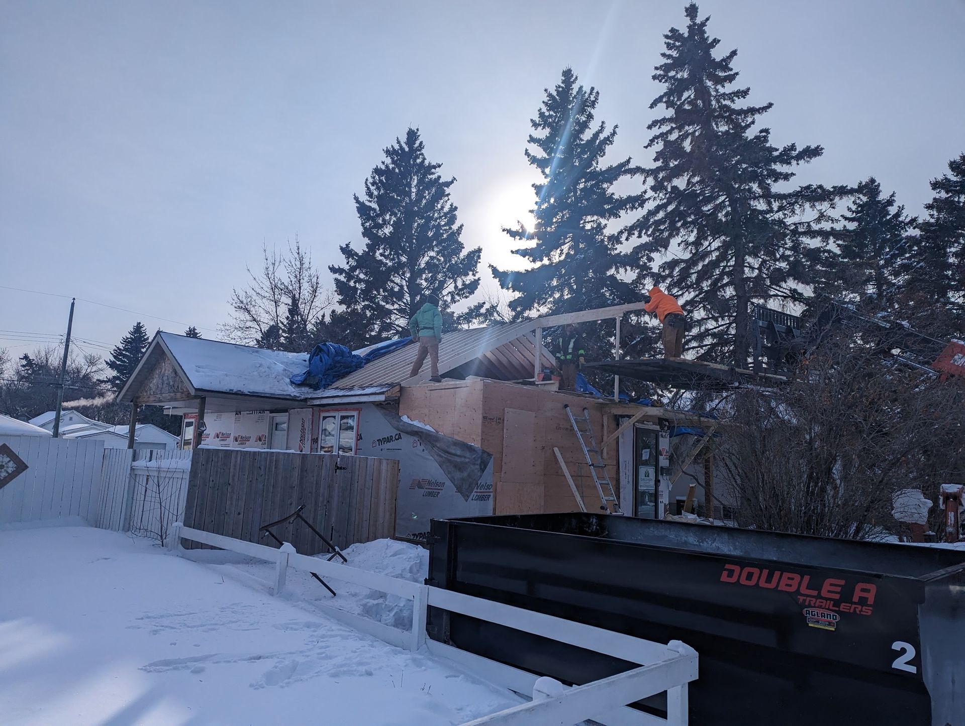 A double r dumpster is parked in front of a snowy house.