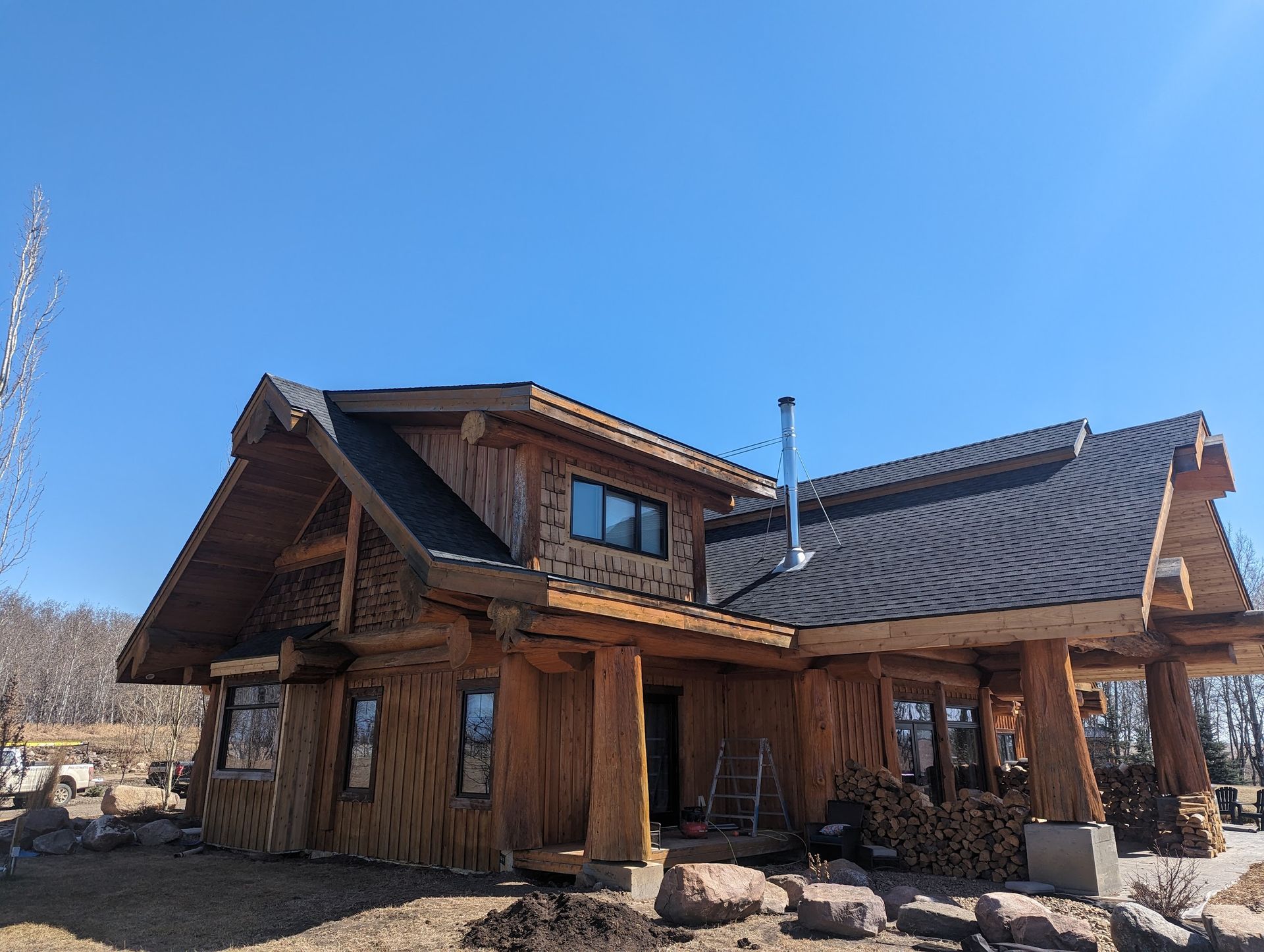 A large wooden house with a black roof is sitting on top of a dirt field.