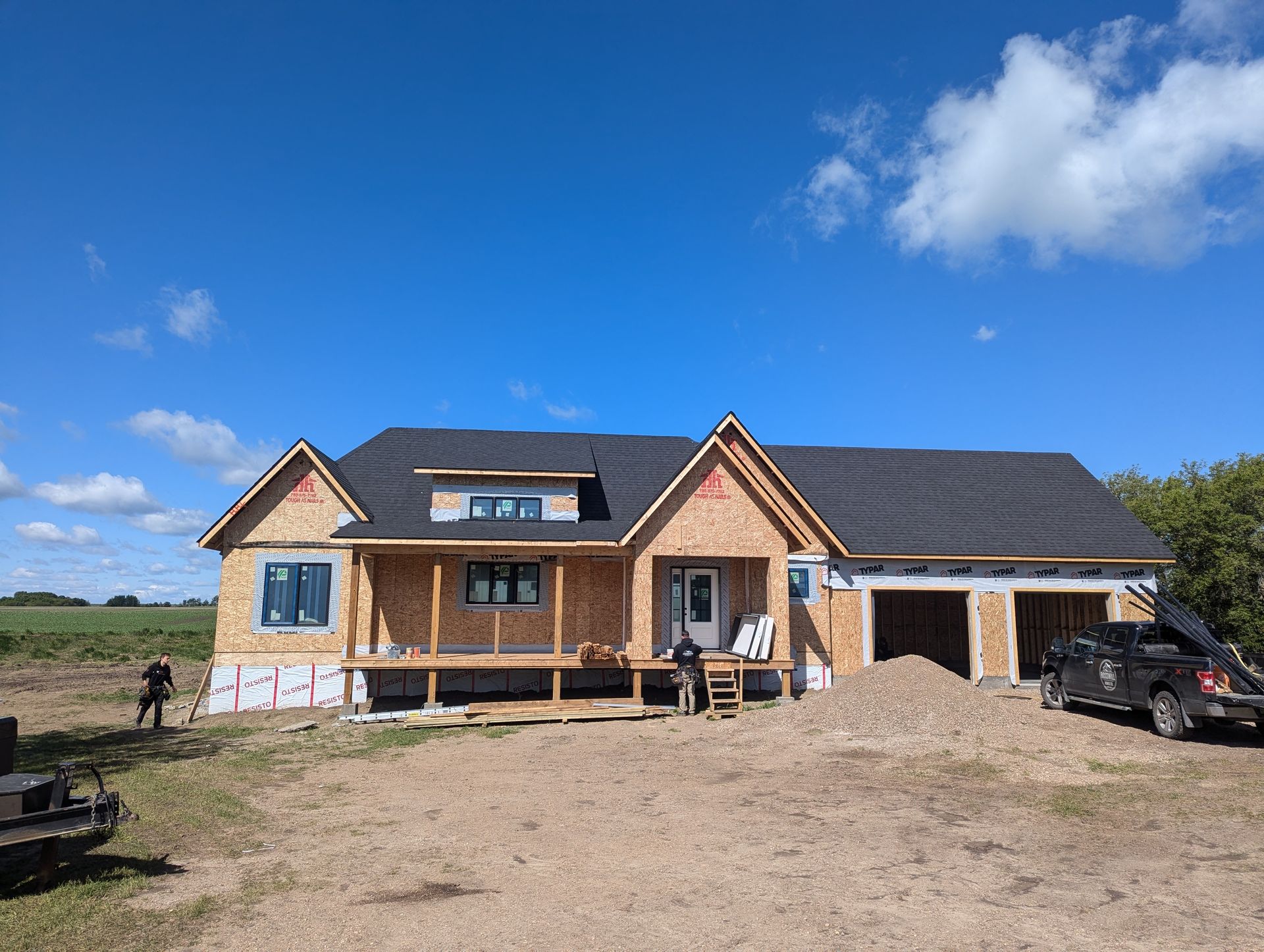 A house is being built in a dirt field with a truck parked in front of it.