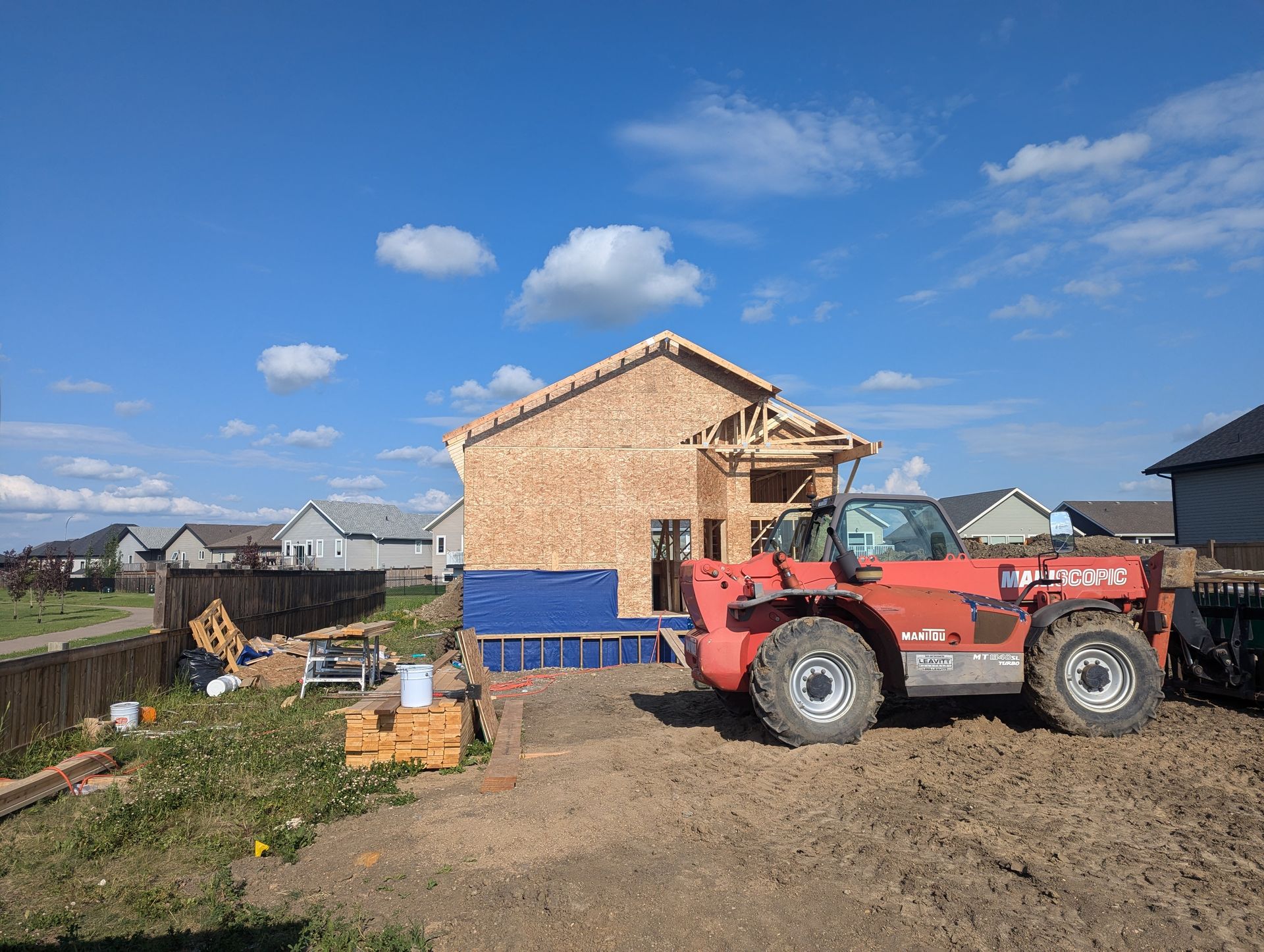 A red forklift is parked in front of a house under construction.