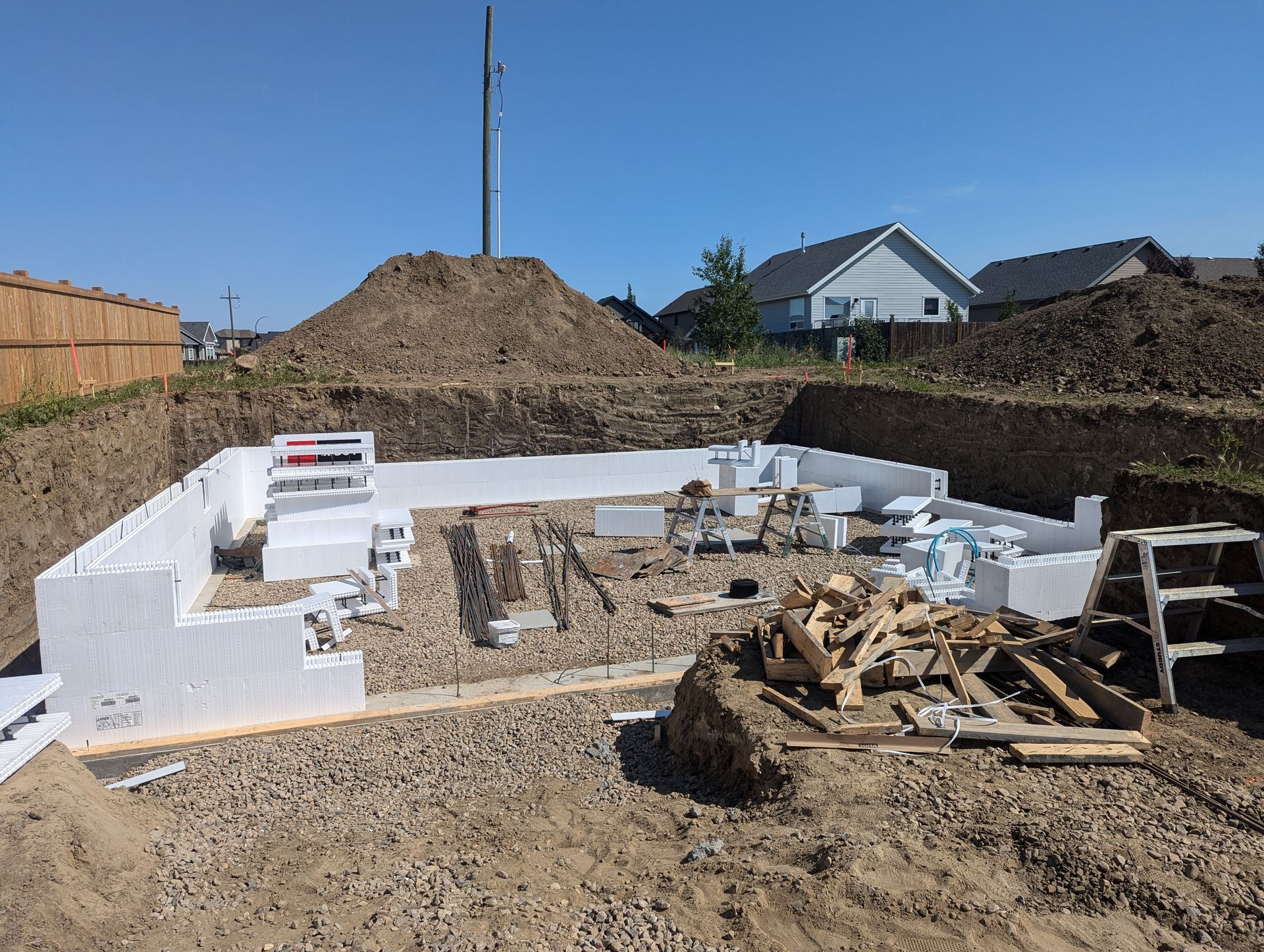 A construction site with a pile of dirt and a house in the background.