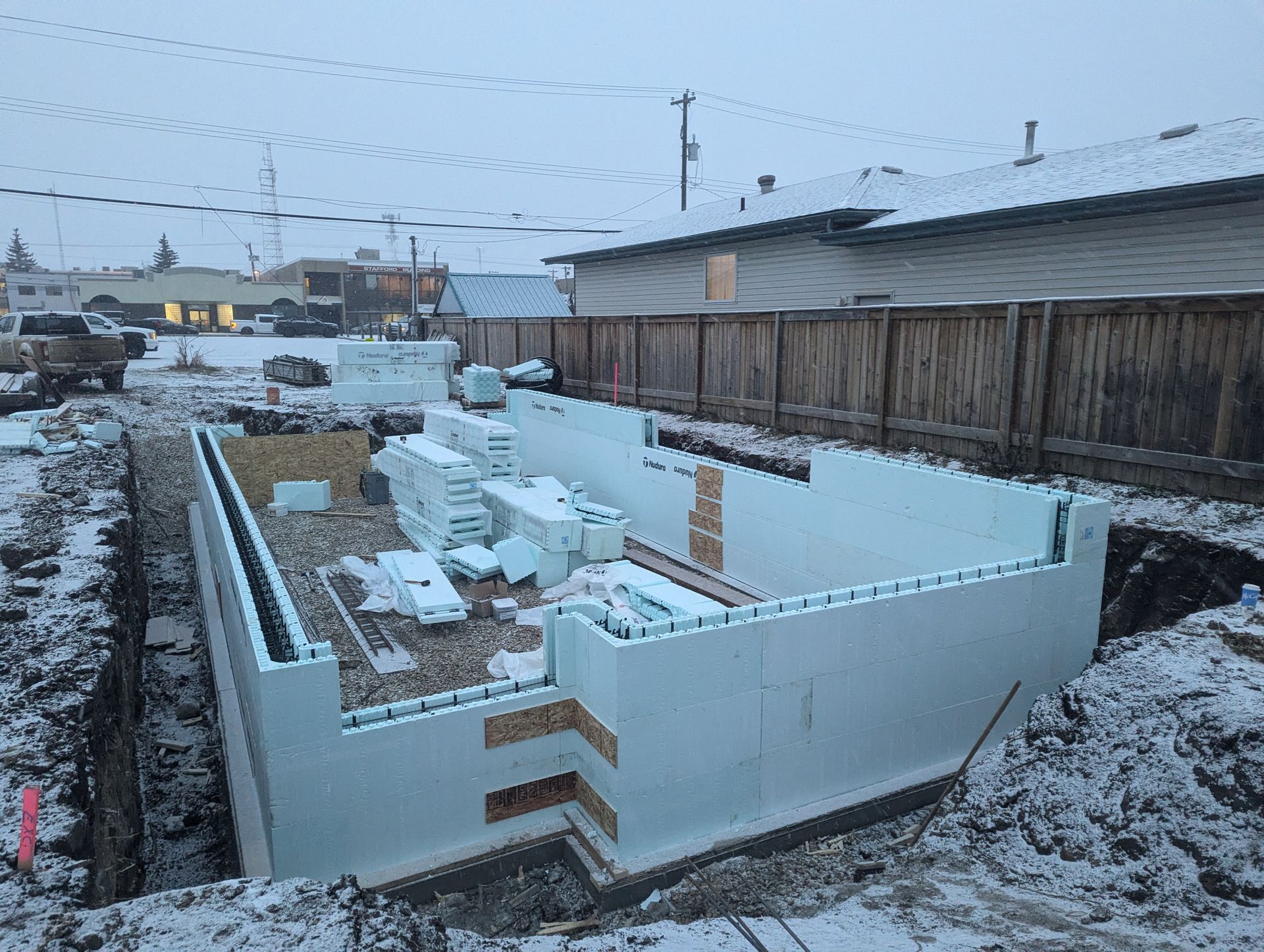 Foundation of a building under construction, made with white insulated concrete forms, surrounded by snow and dirt.