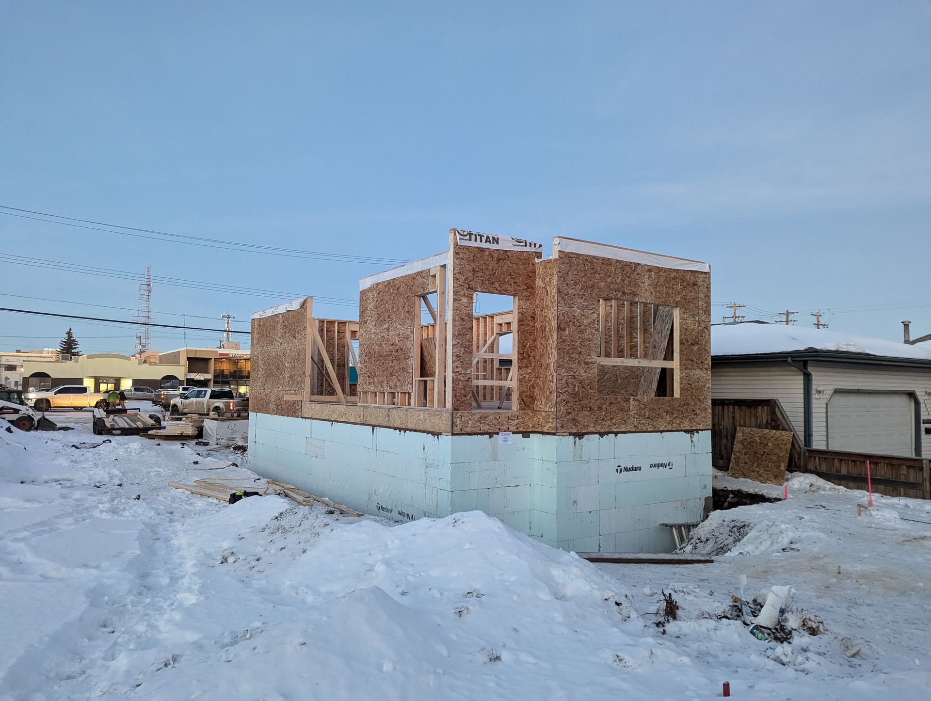 Construction of a house: wooden frame walls on a foam-insulated foundation in a snowy setting.