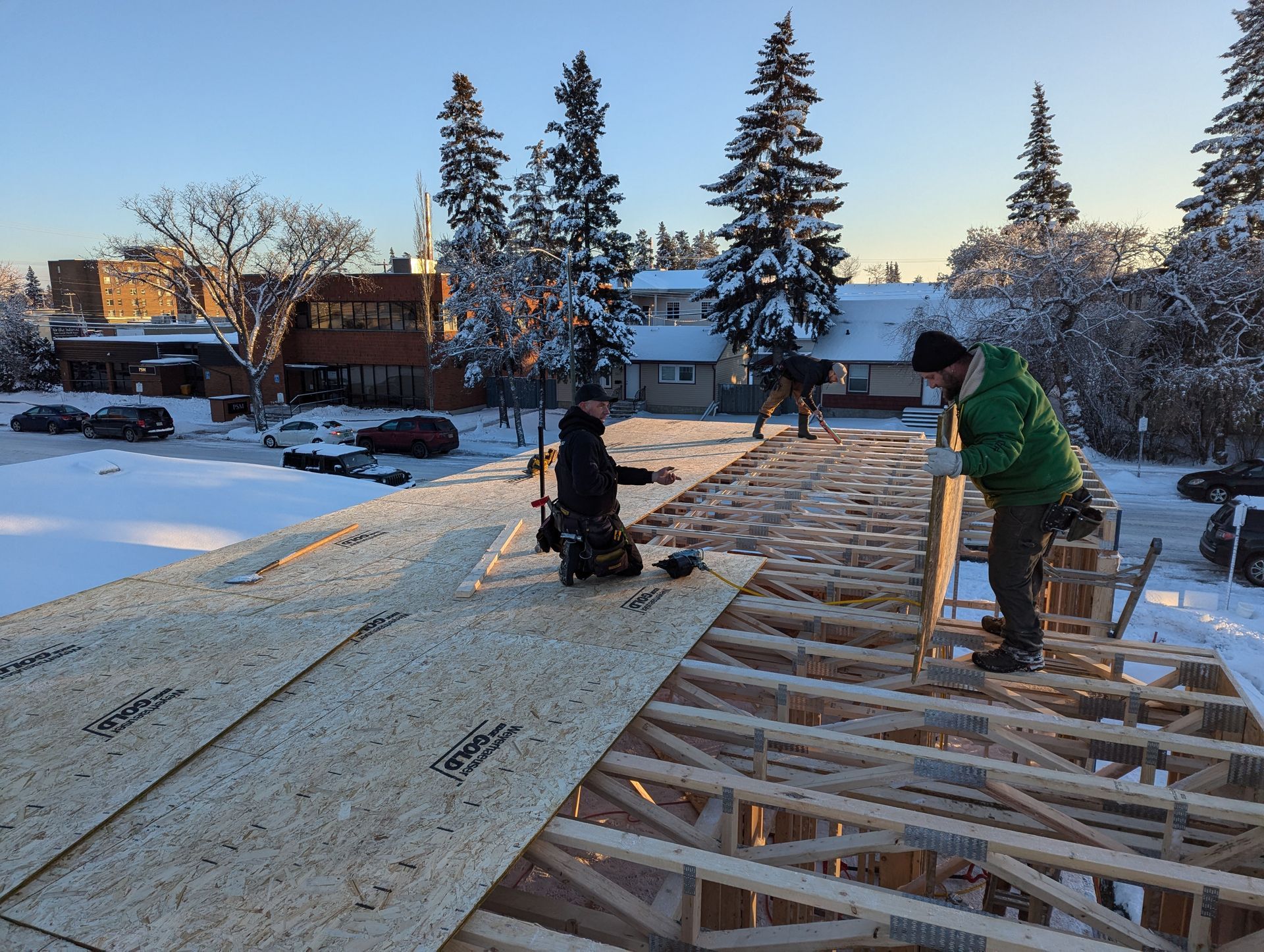 Construction workers installing plywood on a roof frame outdoors on a snowy day.
