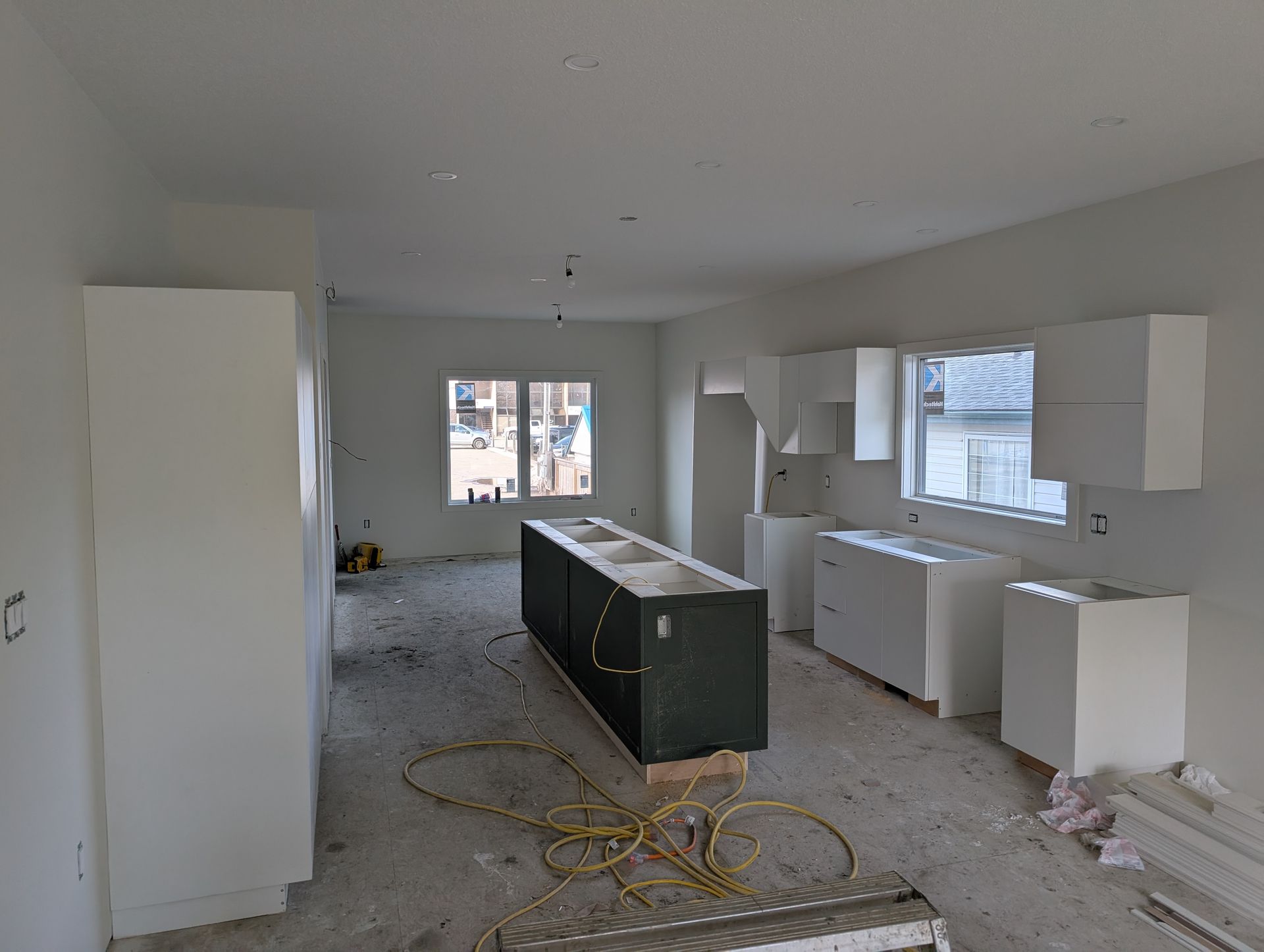 Kitchen under construction with white cabinets, dark island, and exposed wiring.