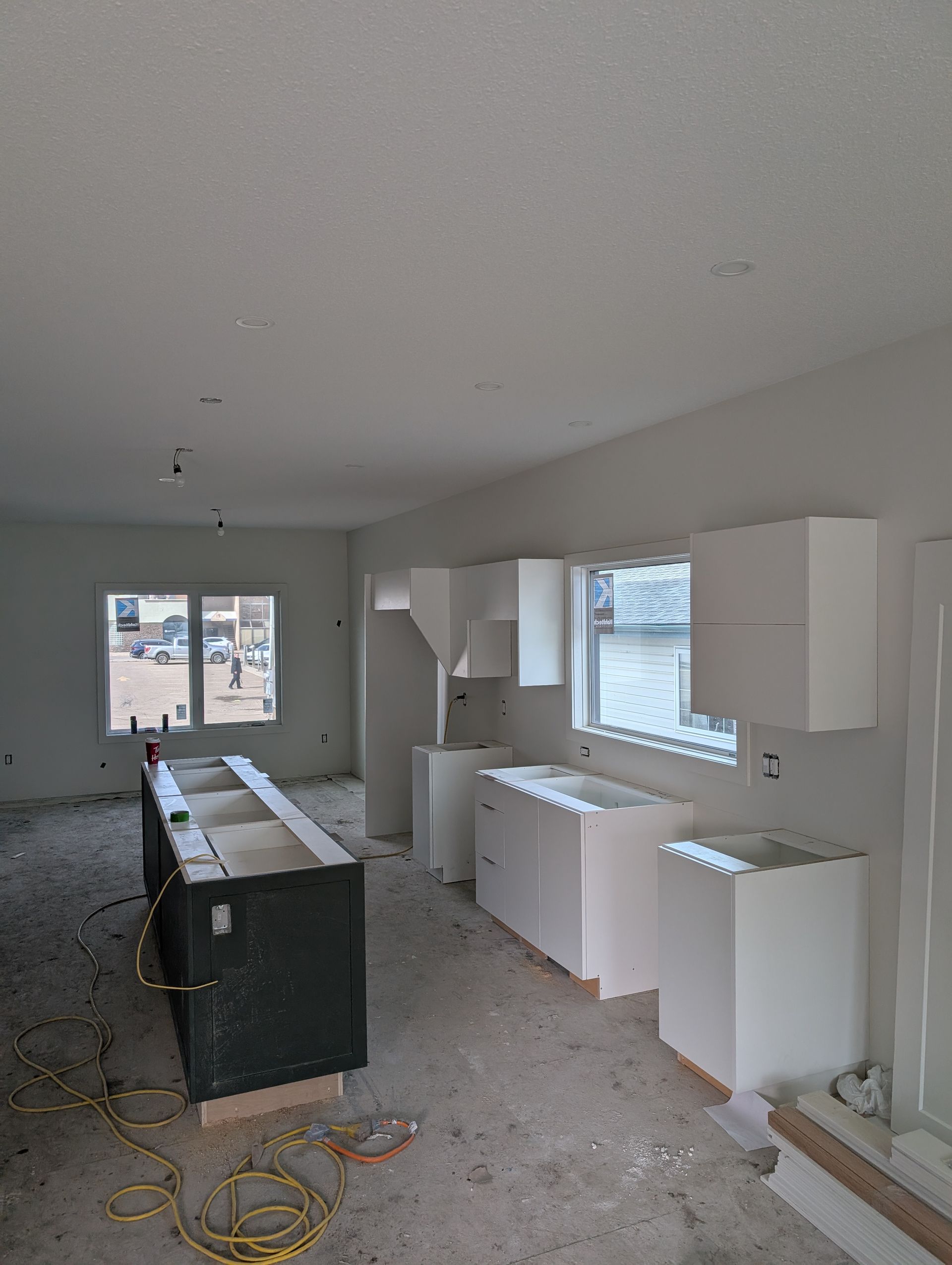 Kitchen under construction with white cabinets and a dark island. Electrical wires are visible.