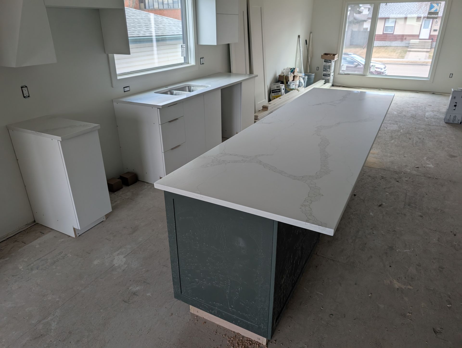 Kitchen under construction, with gray island and white countertops. Cabinets and window are visible.
