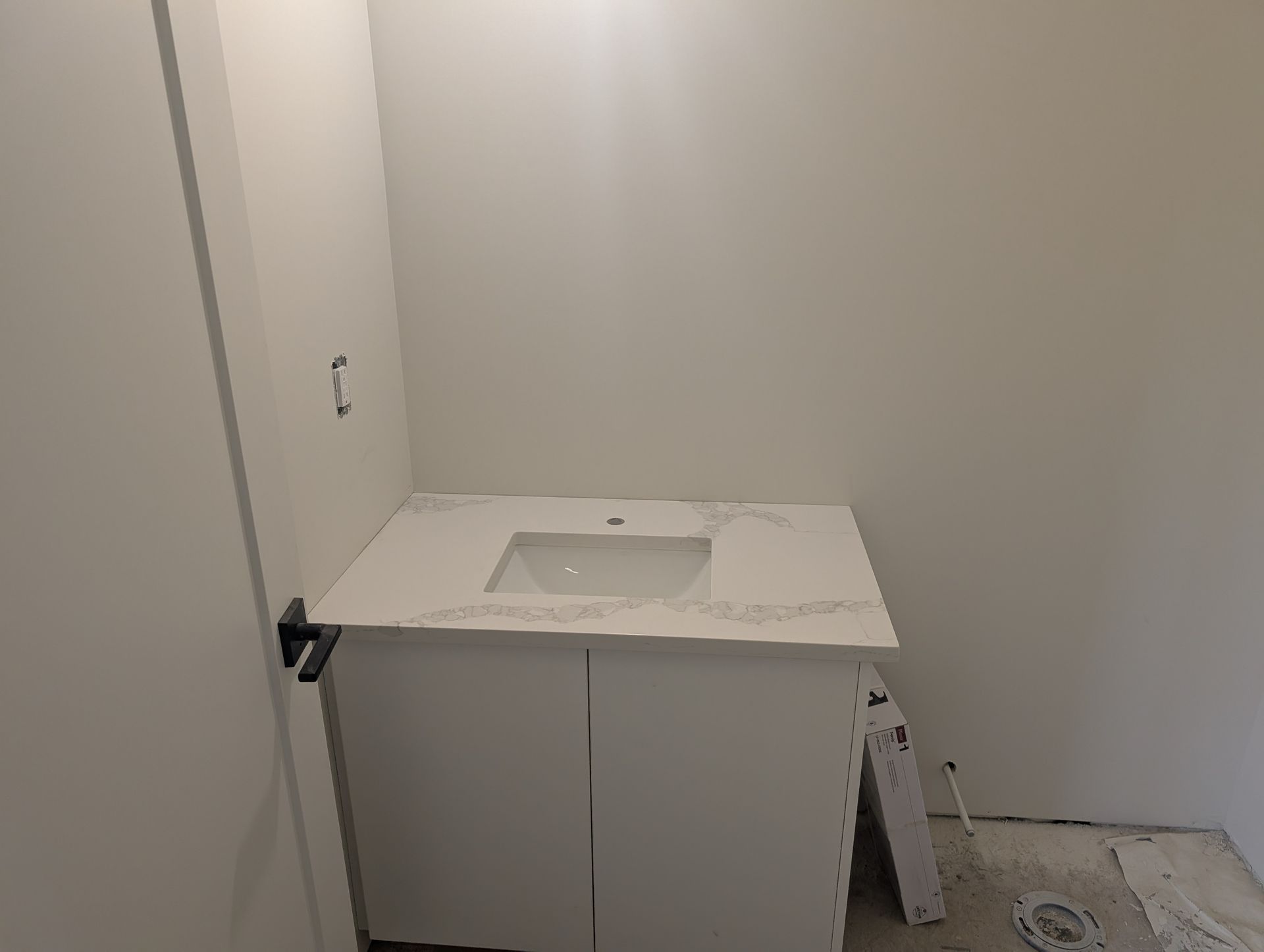 White bathroom vanity with sink and countertop against a white wall; unfinished construction.