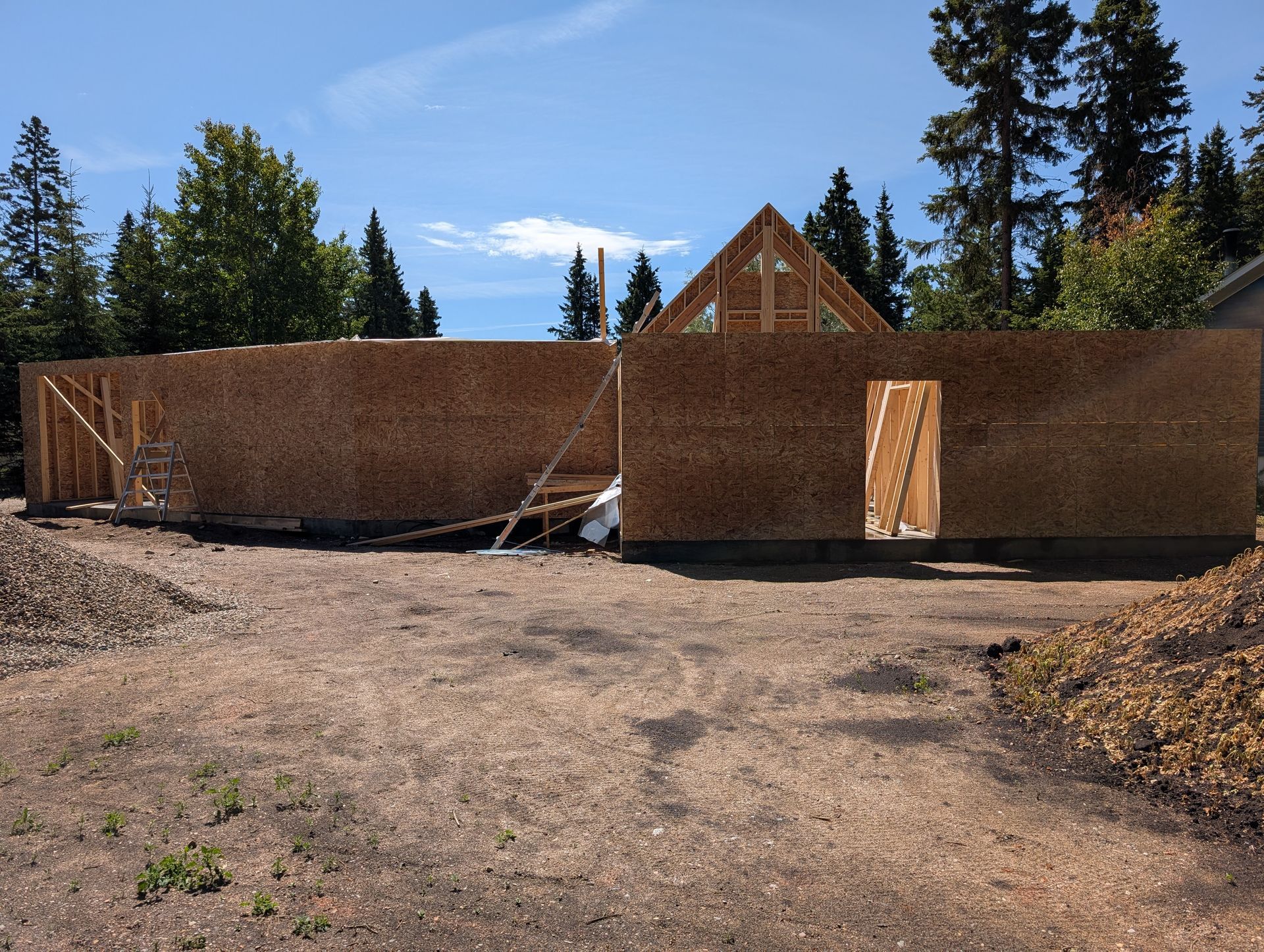 Construction of a building's wooden frame, including walls and roof structure, outdoors under a blue sky.