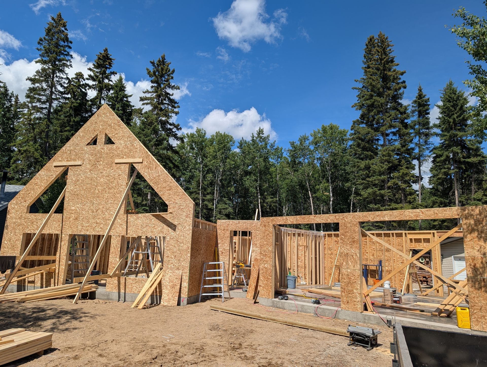 Construction of a house: wooden framework on concrete foundation, blue sky, trees in the background.