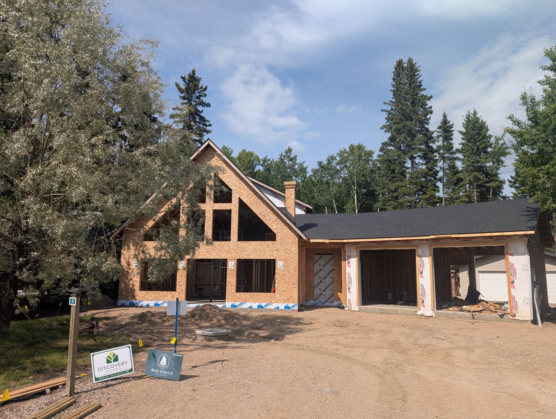 House under construction with exposed wood frame and attached garage under a blue sky.