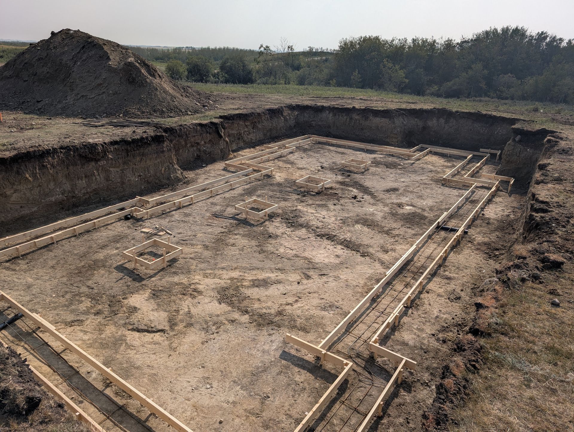 Excavated foundation in a dirt field, with wooden forms outlining the building's shape.