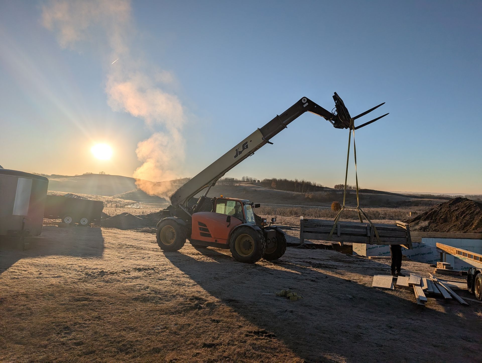 Orange telehandler lifting lumber with a sunny, rural backdrop.