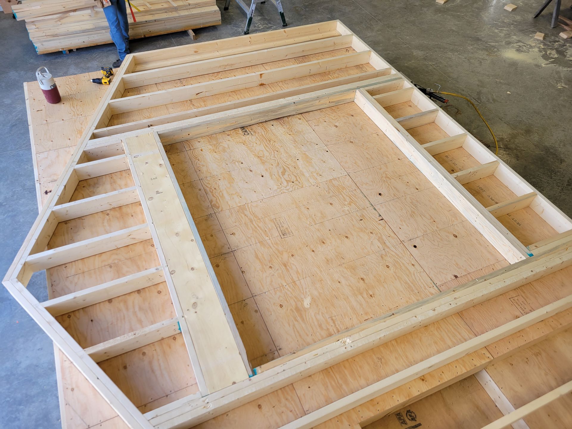 Wooden wall frame construction with triangular and rectangular openings on a plywood base.