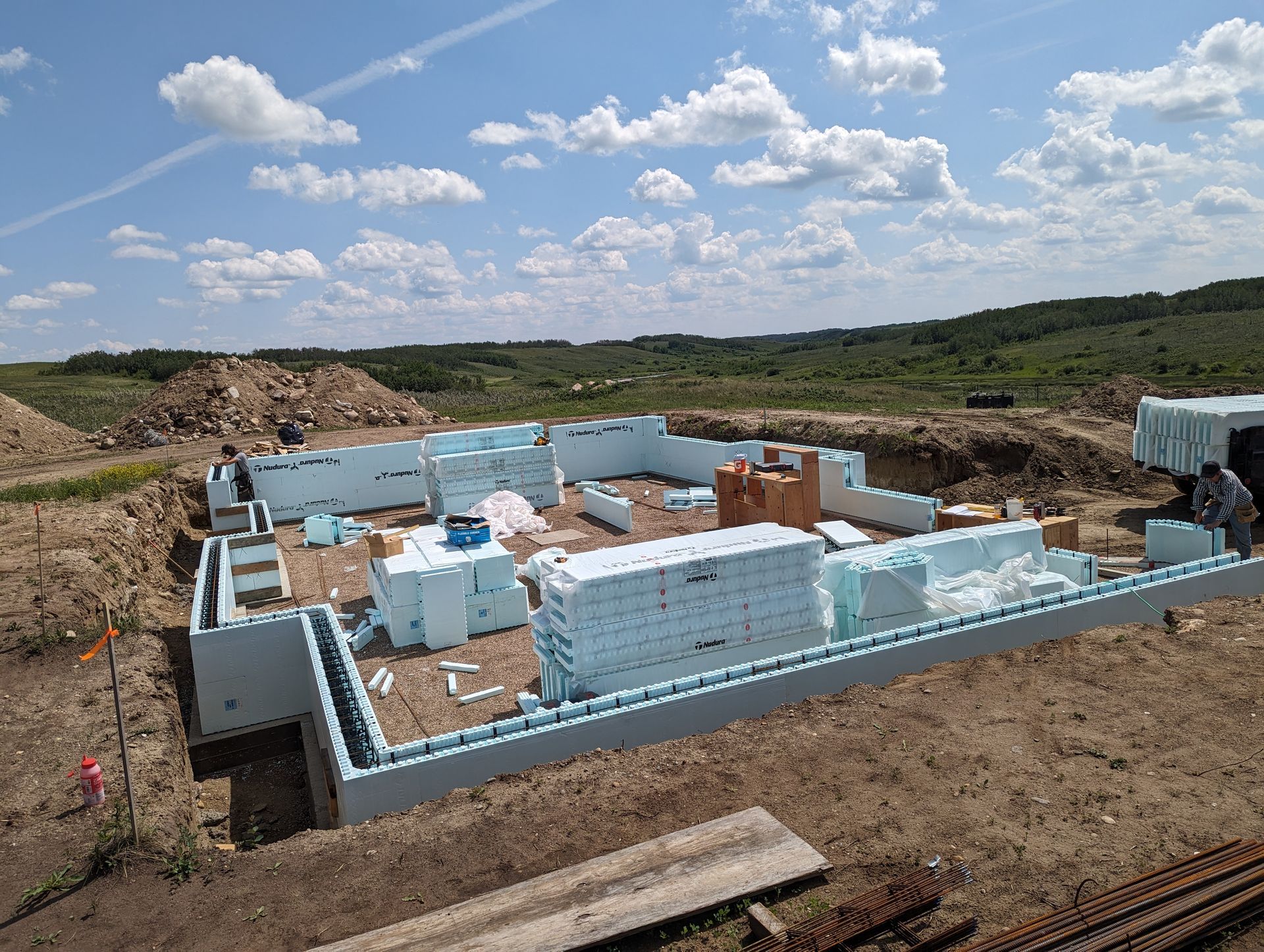 Foundation of a house under construction. Blue insulated foam blocks form the walls. Workers are present on site.
