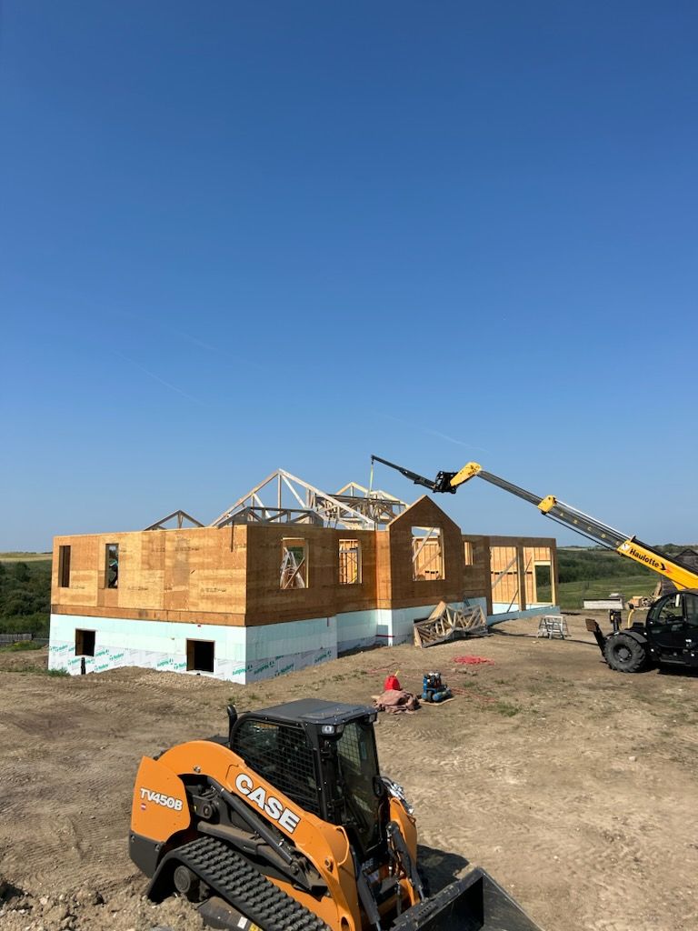 Construction site with a partially framed house, a Case skid steer, and a lift under a blue sky.