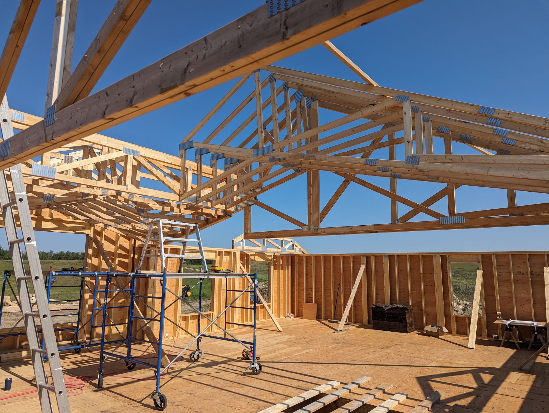 Construction site: wood frame building with trusses under a bright blue sky.