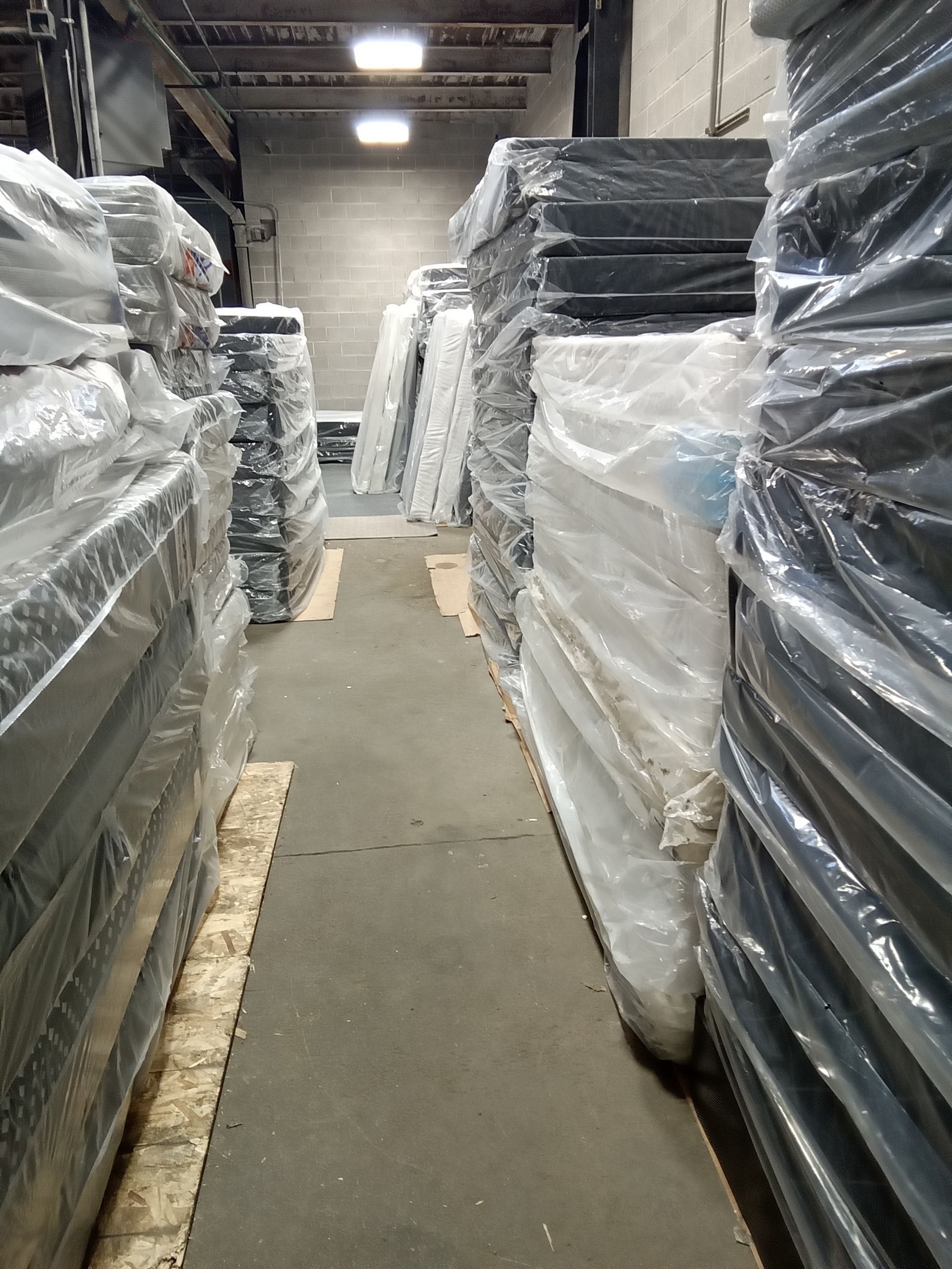 A narrow warehouse aisle lined with plastic-wrapped stacked pallets on both sides.