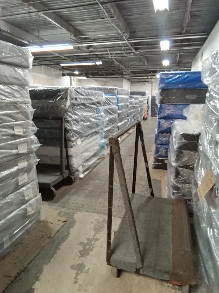 Warehouse aisle with stacked pallets wrapped in plastic and a pallet jack in the foreground