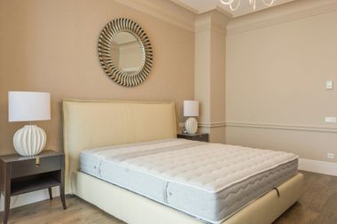 Neat beige bedroom with a bed, two lamps, and a round wall mirror