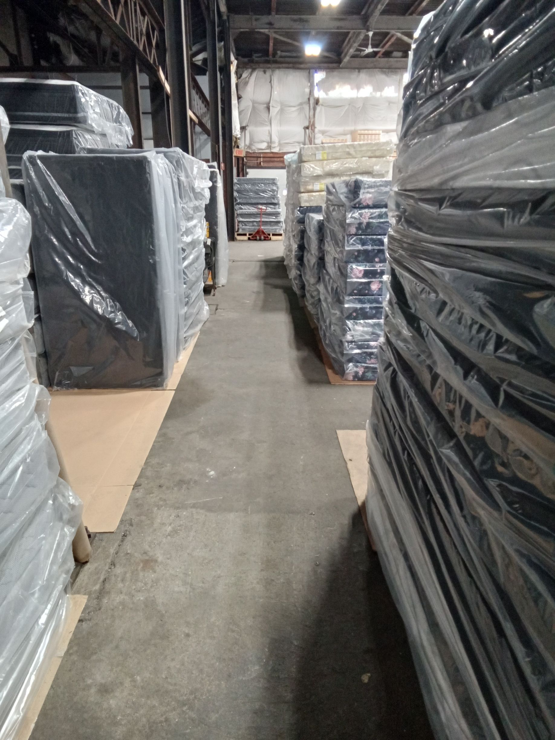 A warehouse aisle with large black-wrapped pallets stacked along both sides.