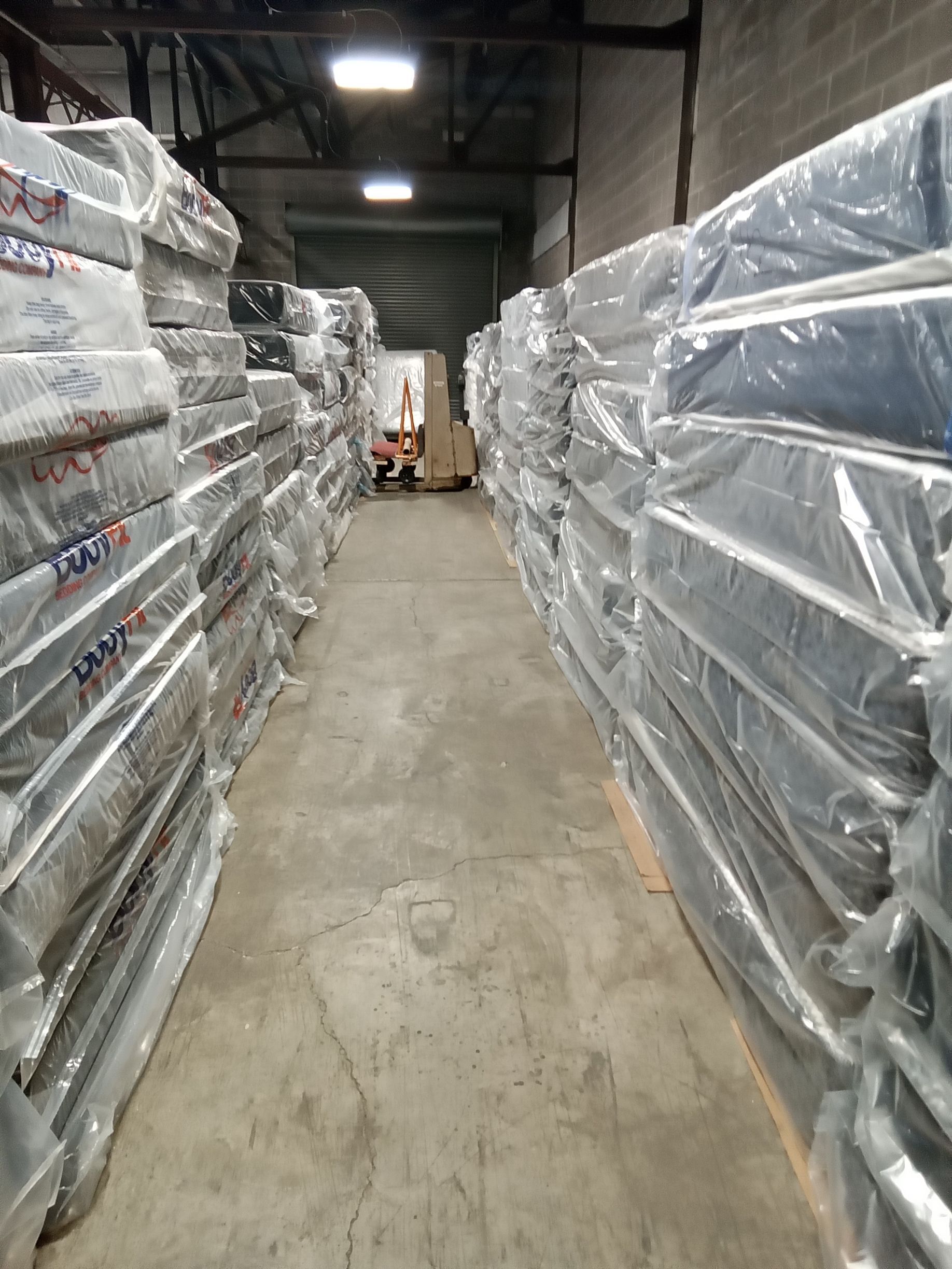 Warehouse aisle with tall stacks of shrink-wrapped pallets on both sides and a forklift in the distance