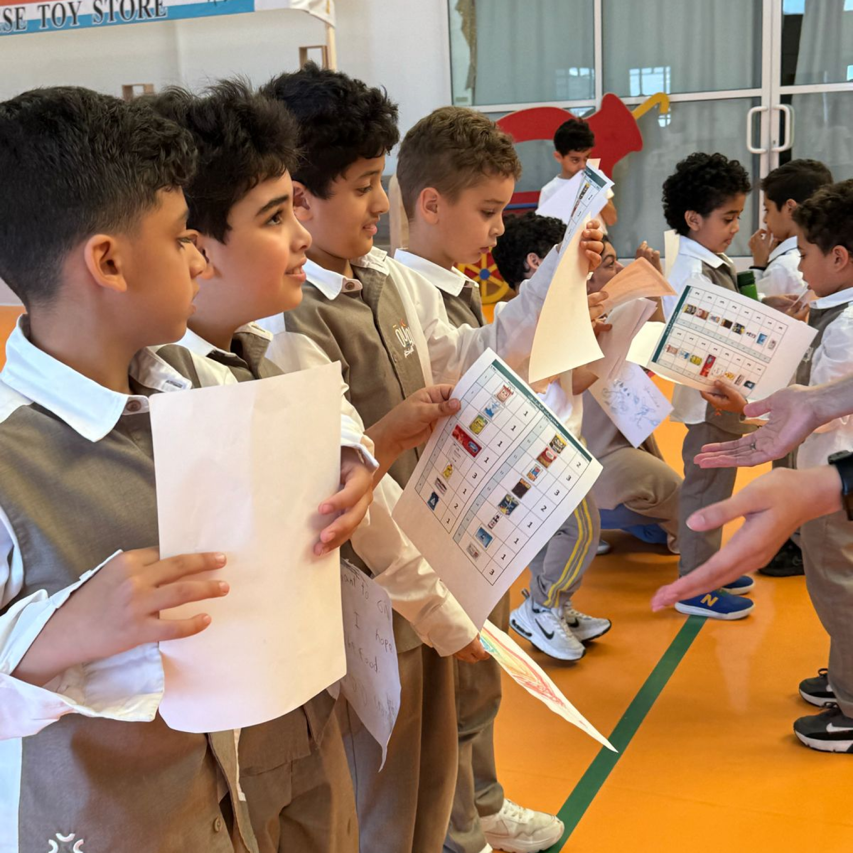 A group of young boys are standing in a line holding papers