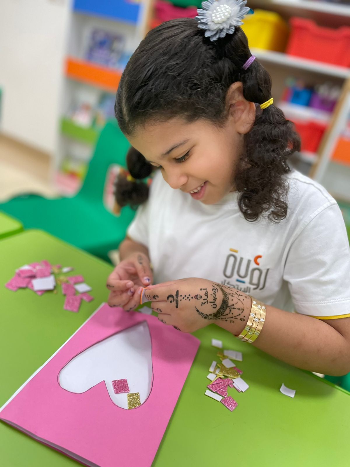 A little girl is sitting at a table making a heart out of paper.