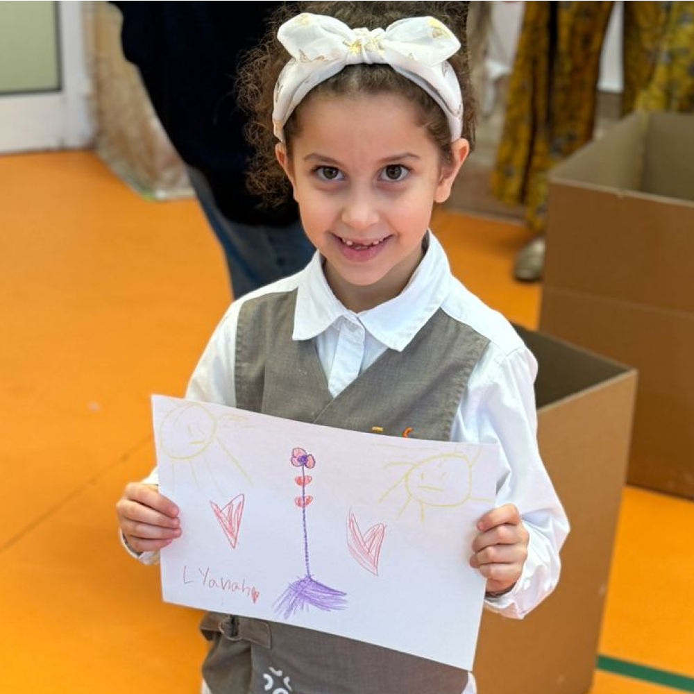 A little girl is holding a piece of paper with a flower drawn on it