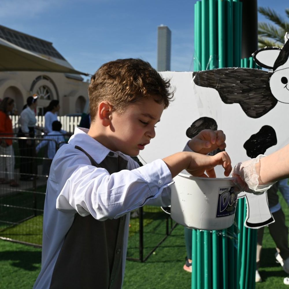 A young boy is pouring milk into a bucket in front of a cow statue