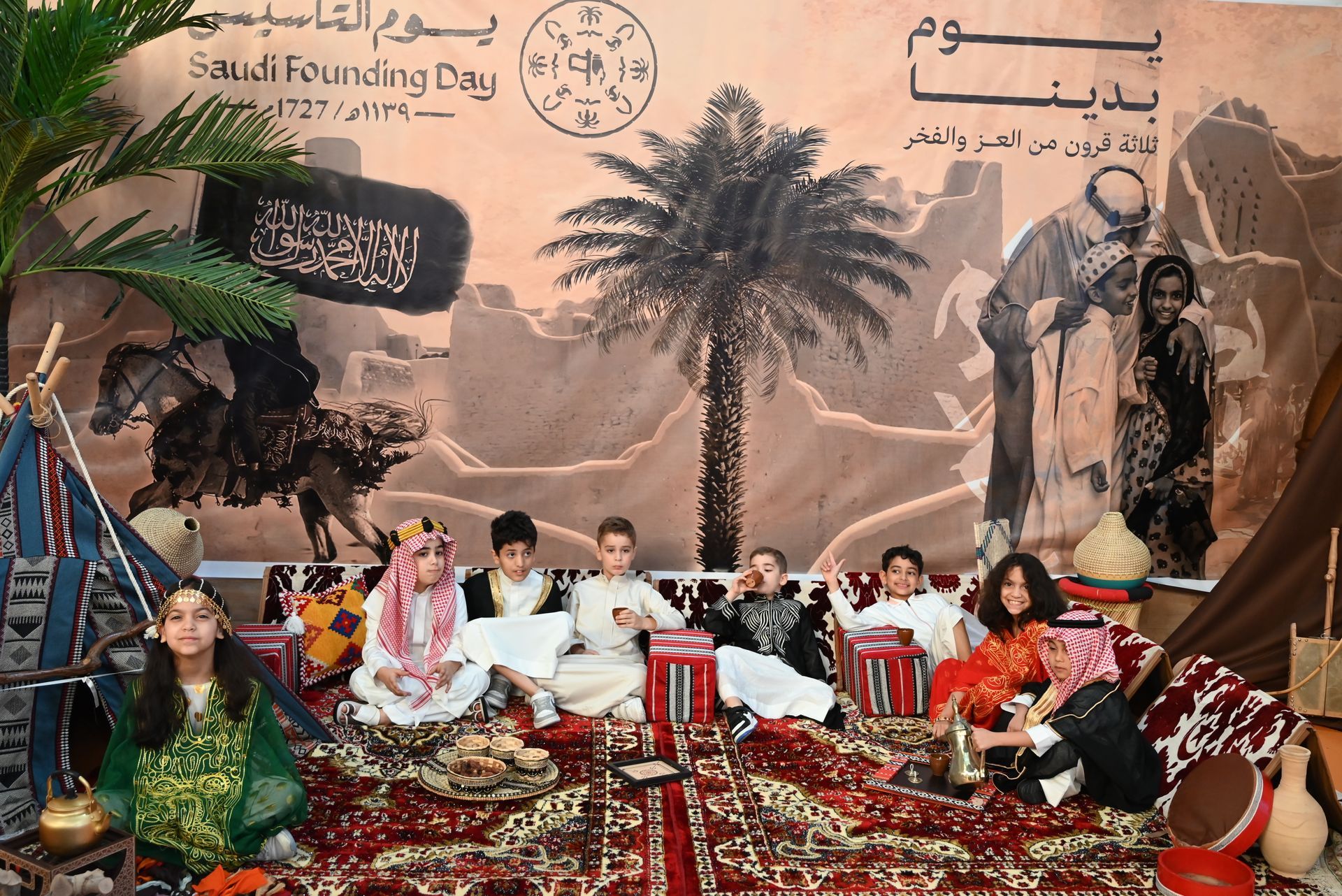 A group of children are sitting on a rug in front of a wall with arabic writing on it