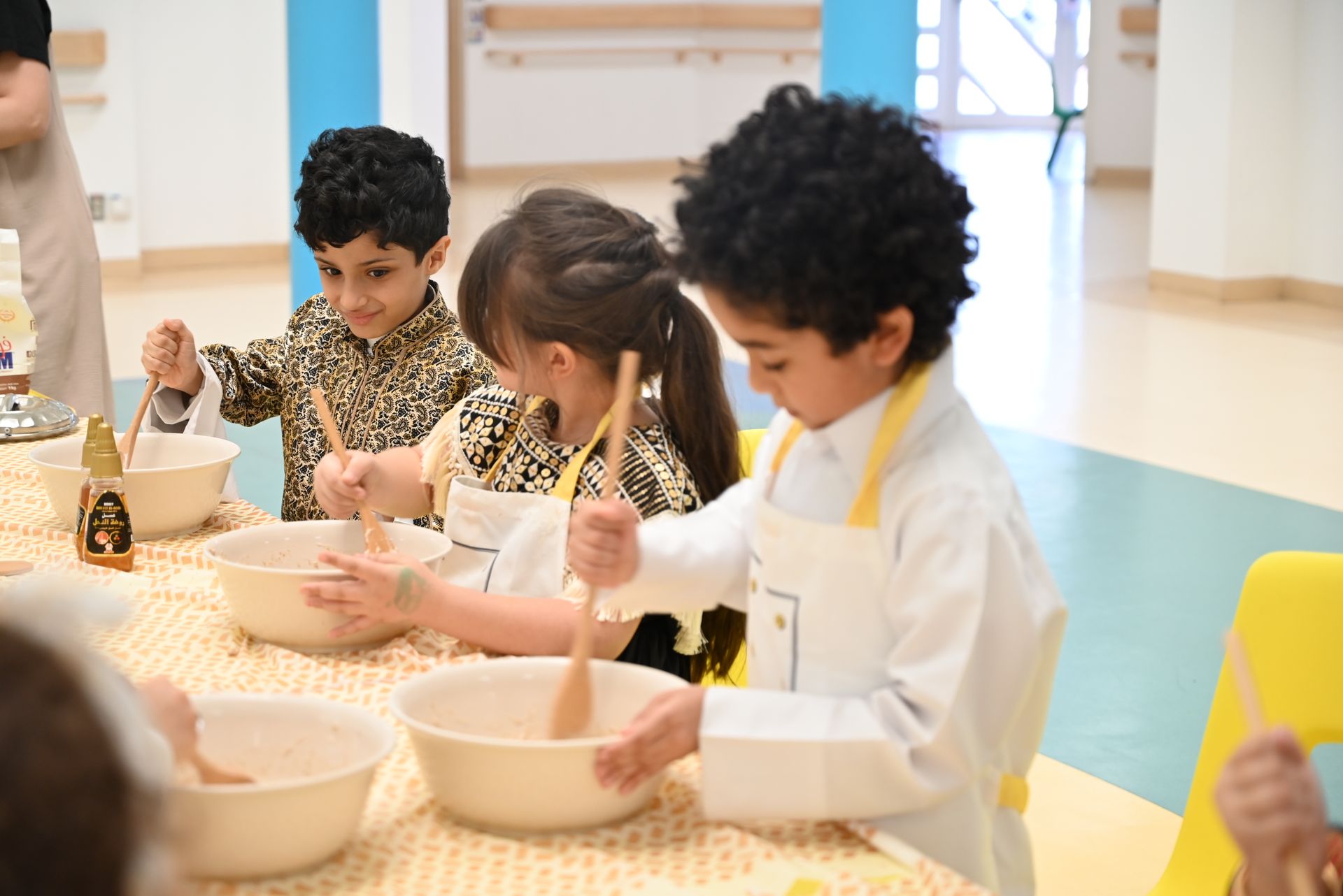 A group of children are sitting at a table mixing ingredients in bowls.