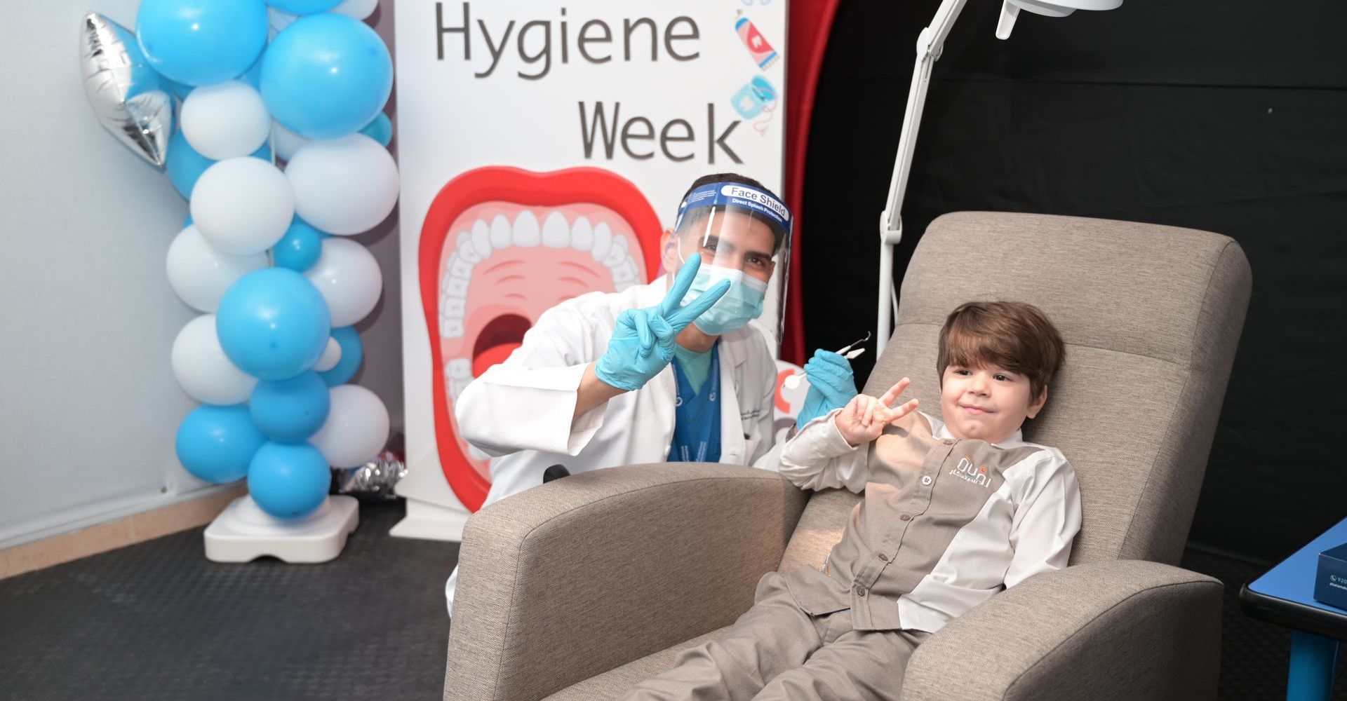 A boy is sitting in a chair in front of a sign that says dental hygiene week