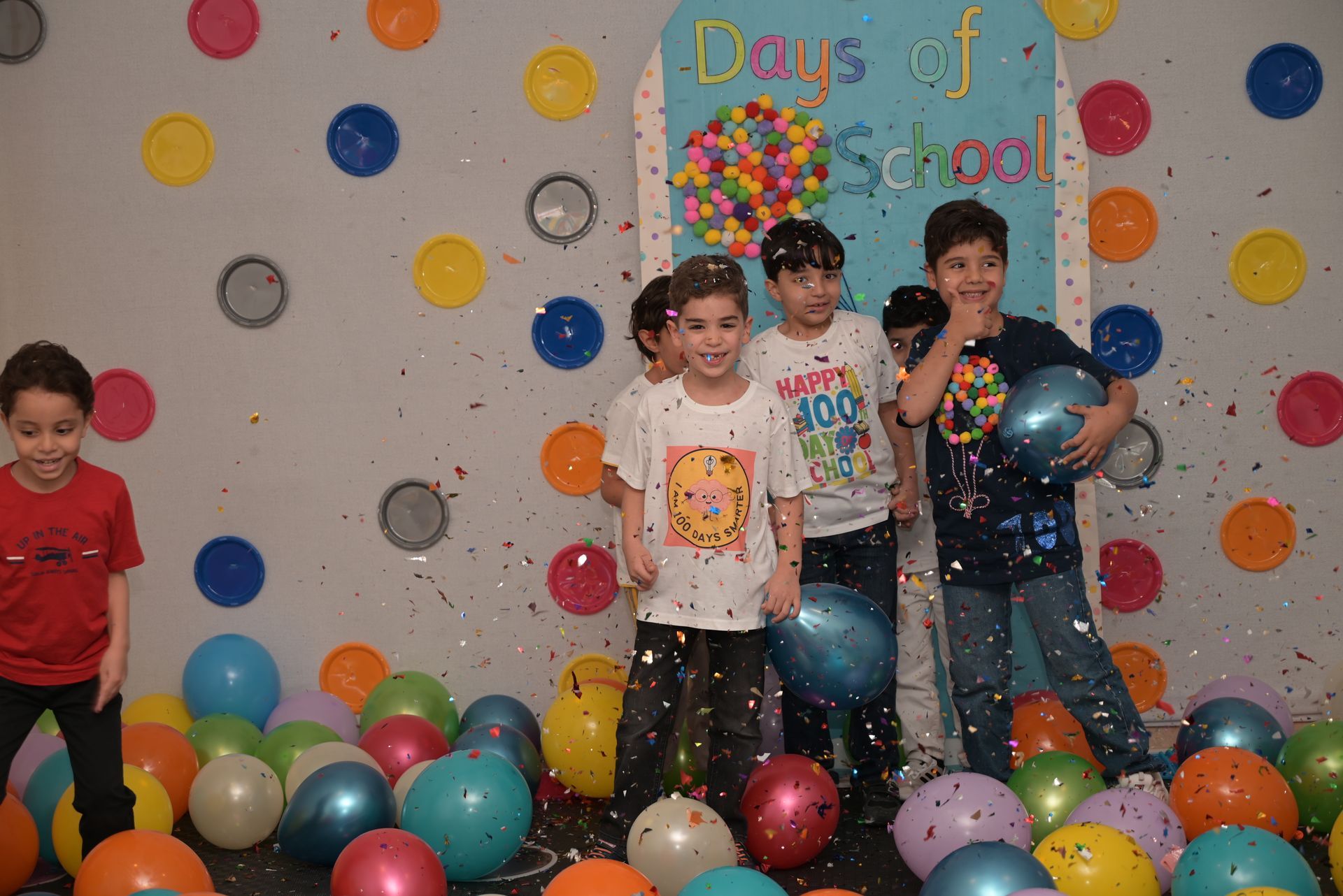 A group of children are standing in front of a wall covered in balloons.