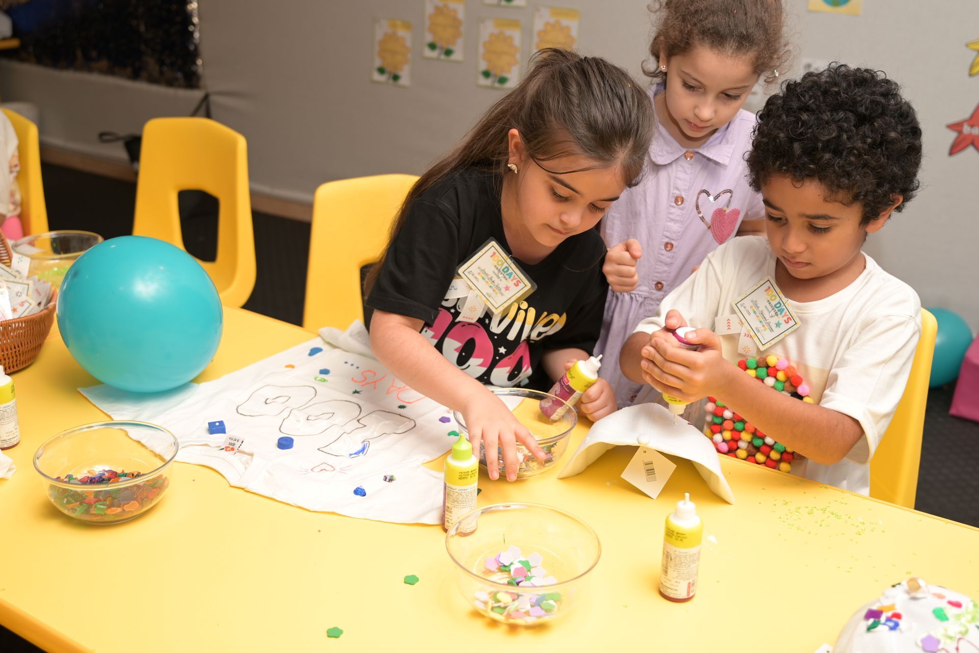 Three children are sitting at a table playing with sprinkles.