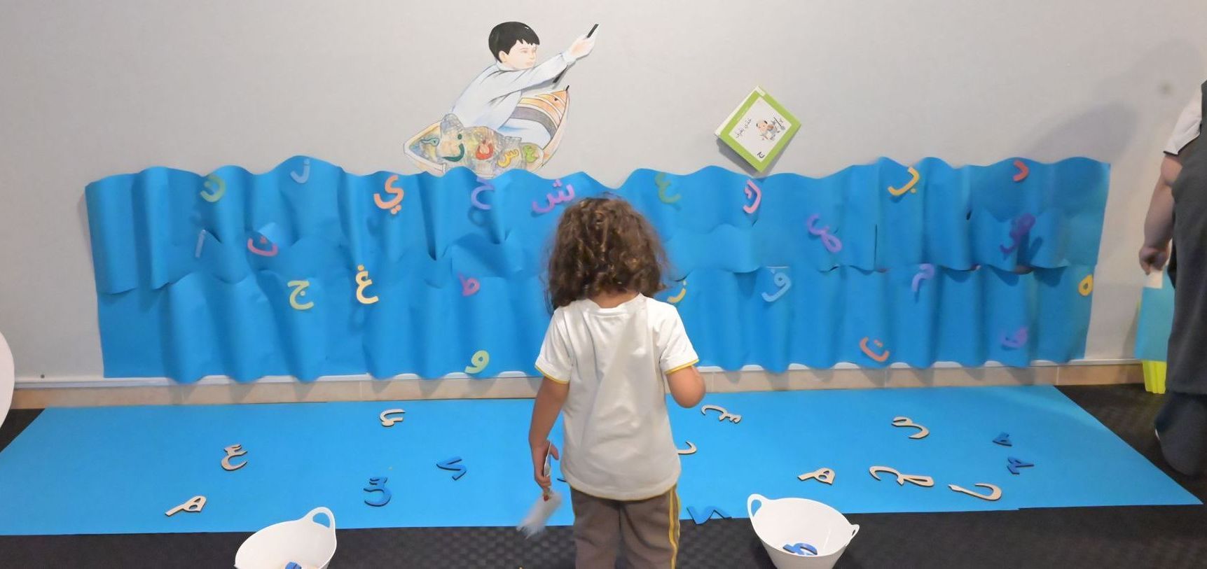 A little girl is standing in front of a wall with letters on it.