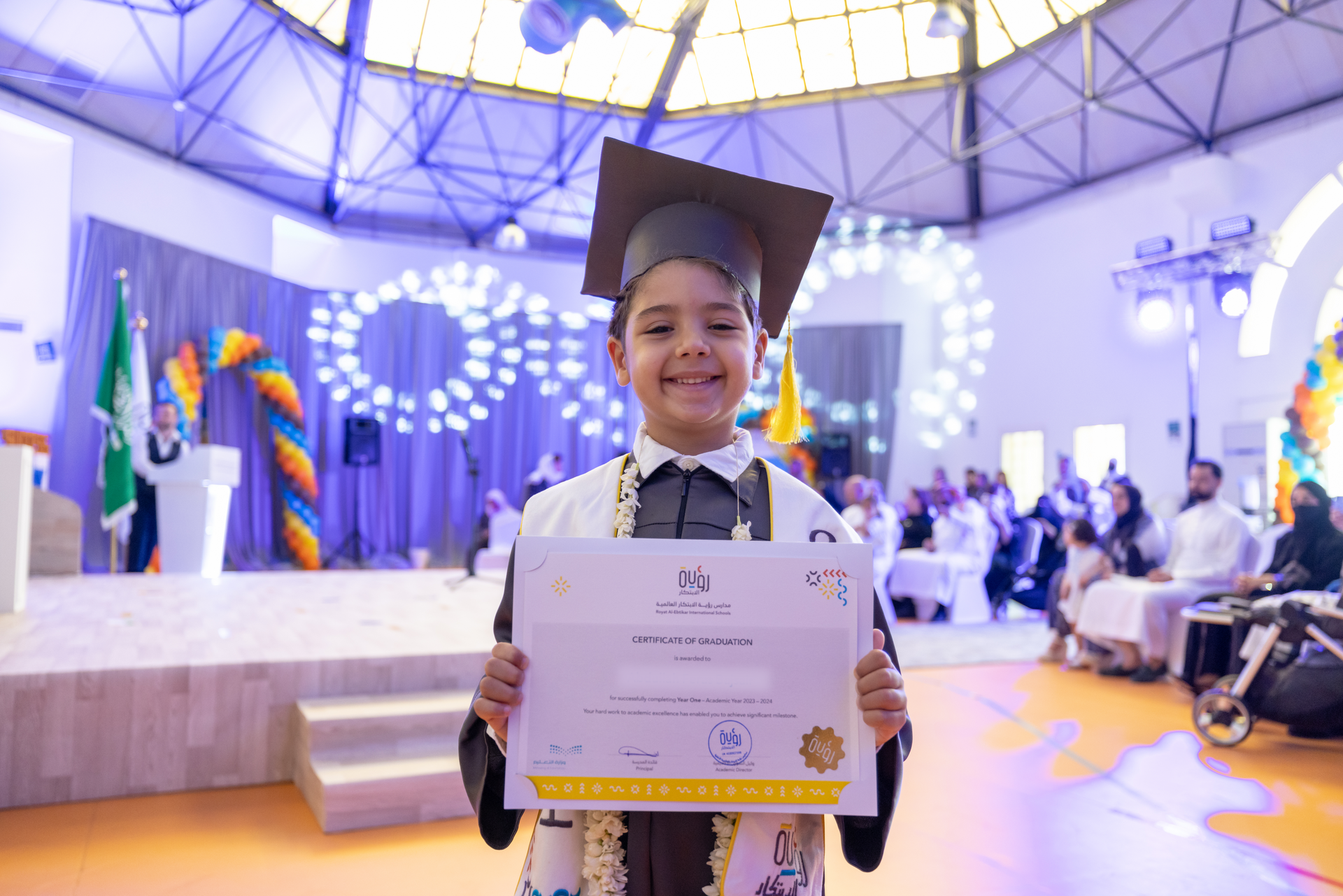 A young boy in a graduation cap and gown is holding a certificate.