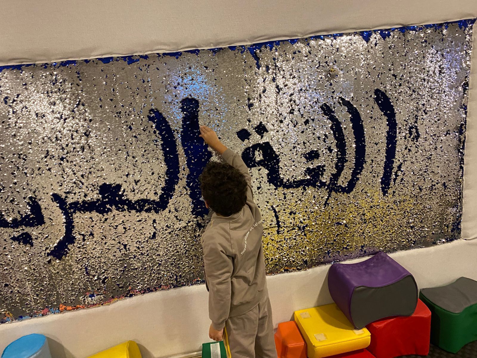 A child is standing in front of a wall with arabic writing on it