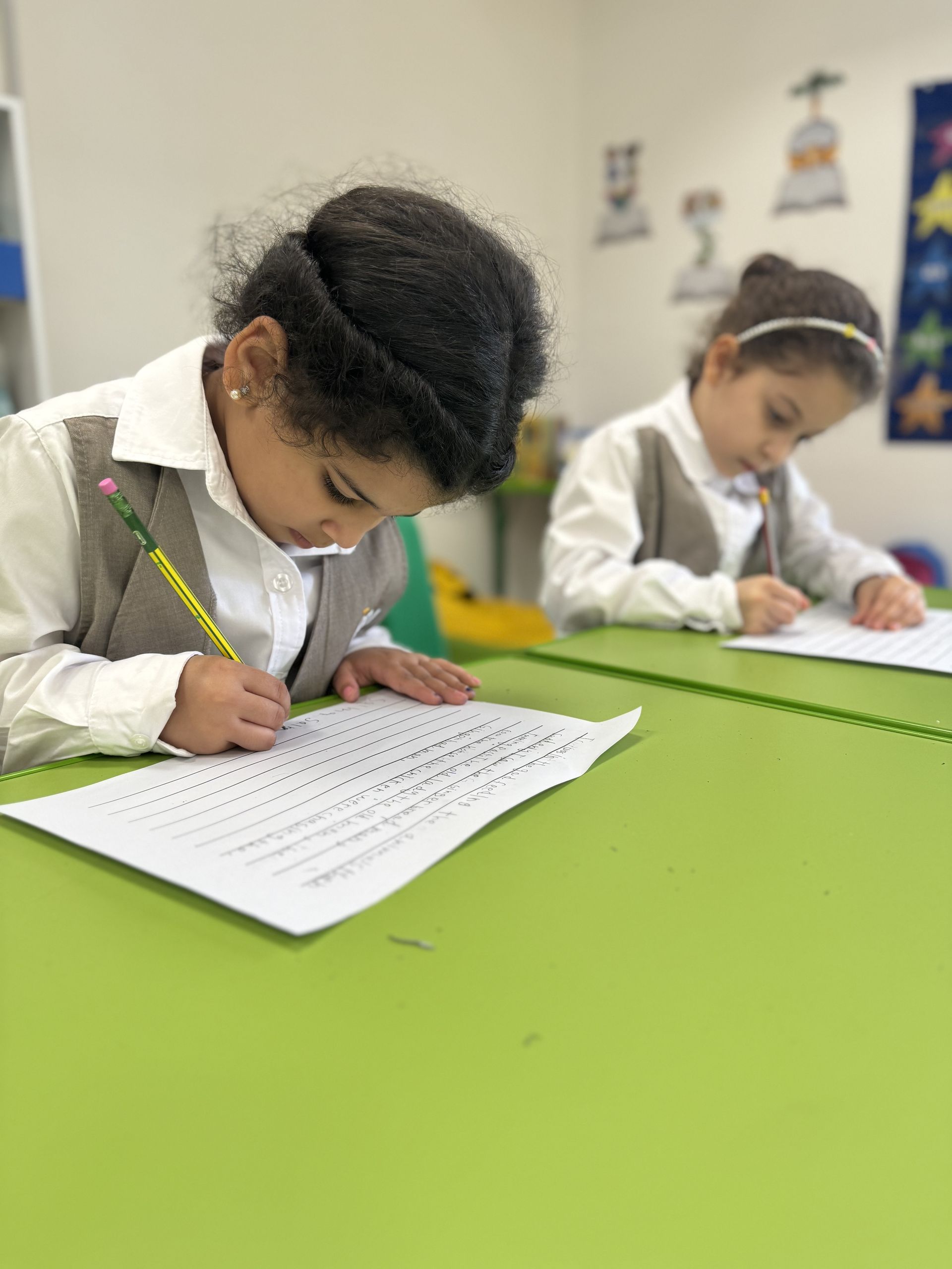 Two students are sitting at a table writing on a piece of paper.